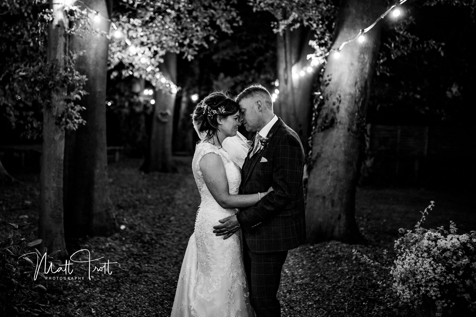 bride and groom holding each other outside in the trees with fairy lights at night at crown lodge kent