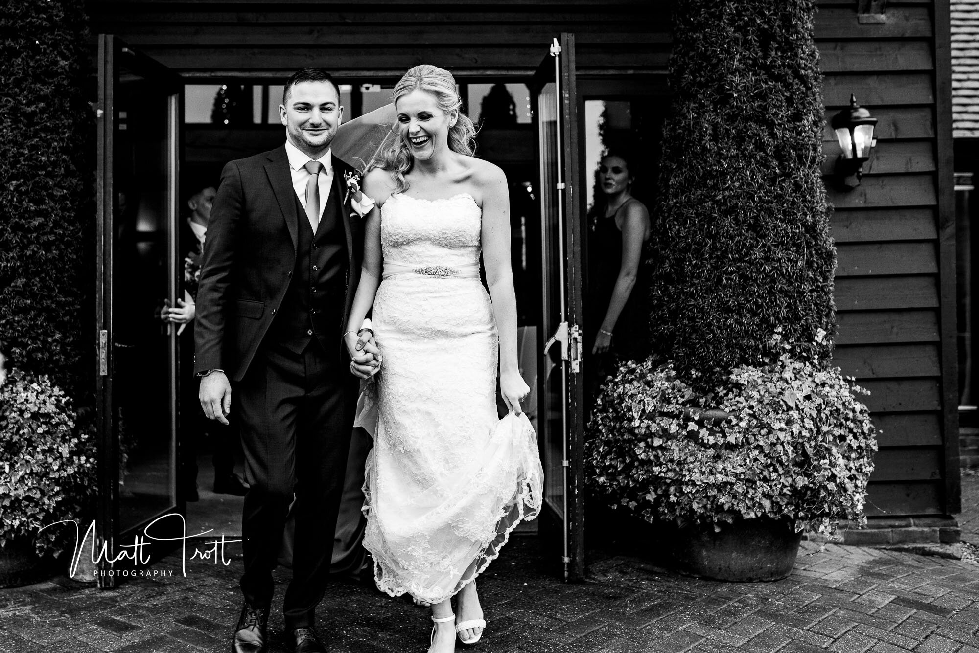 Bride and groom laughing as they enter the wind and rain at the old kent barn