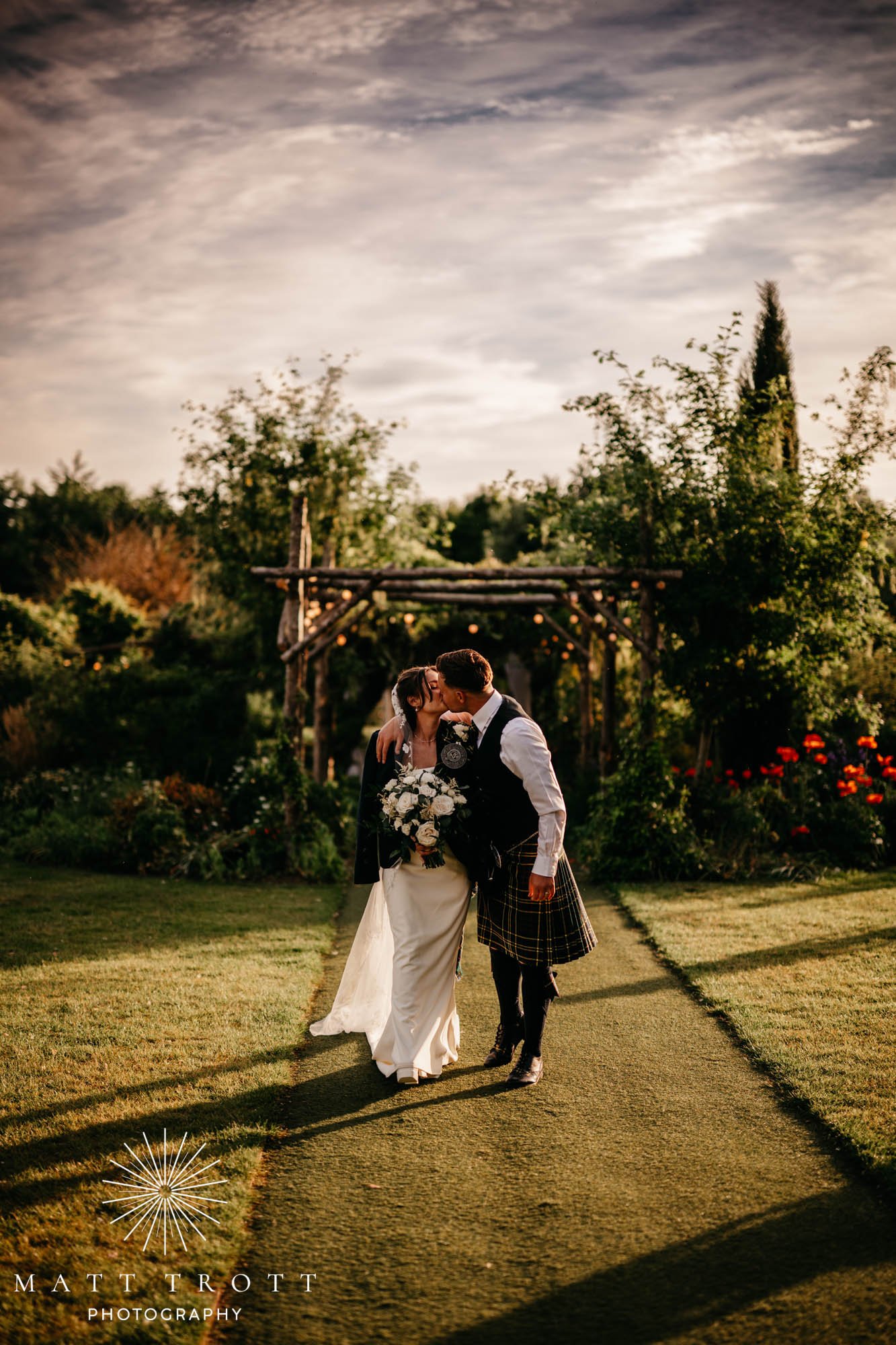 Bride and groom walking and kissing during golden hour at the gardens yalding