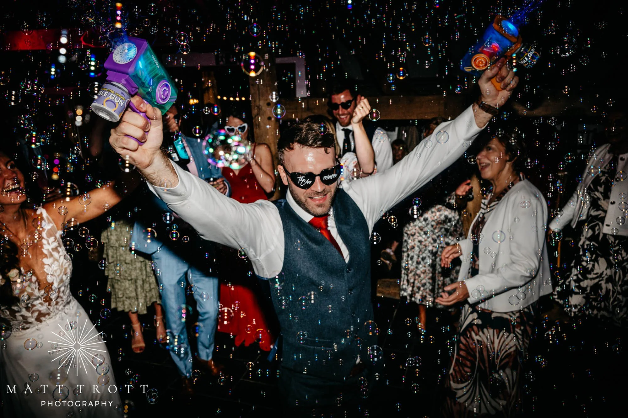 Groom with sunglasses on and two bubble guns filling the dancefloor with bubbles