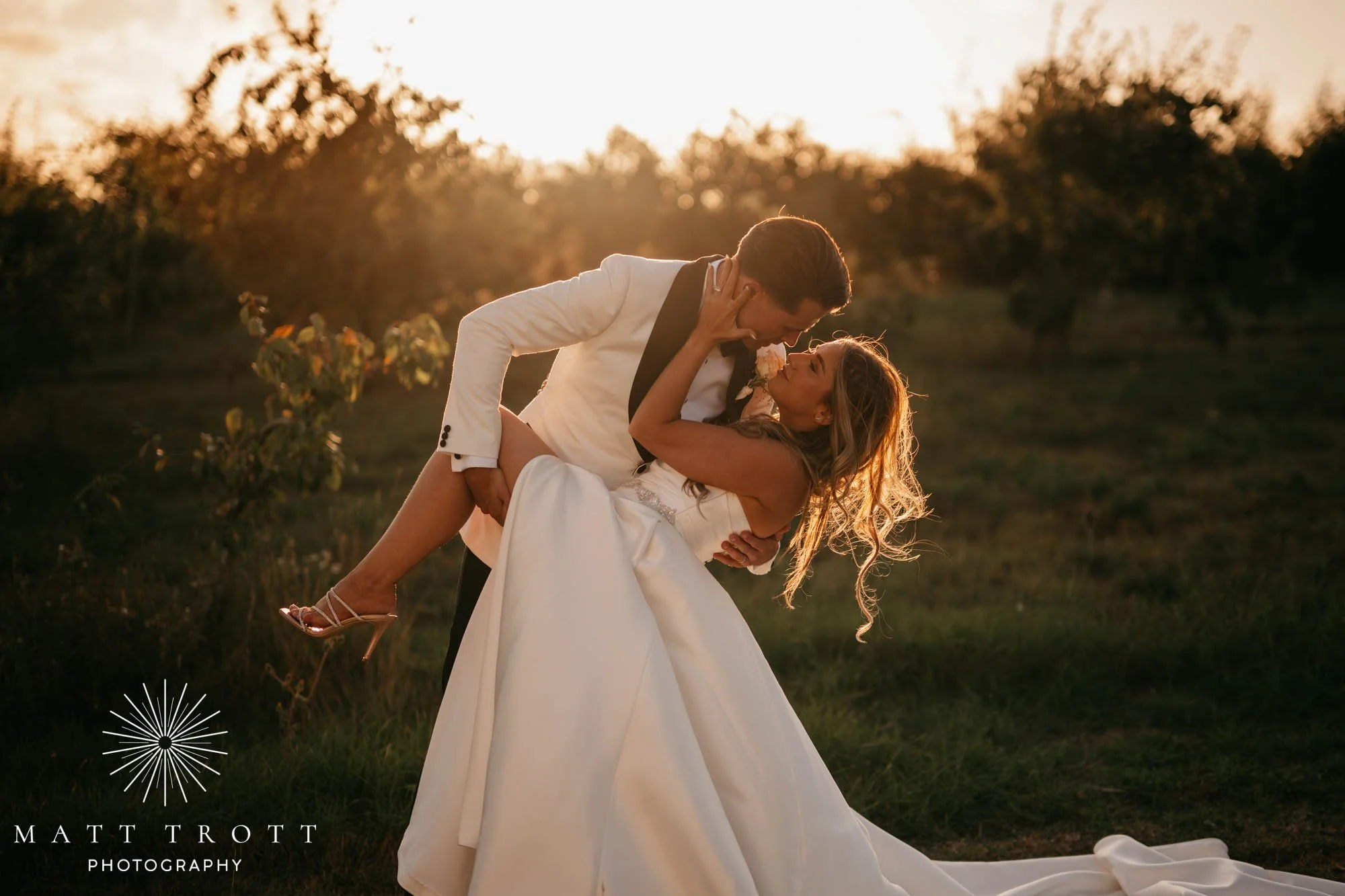 Bride and Groom kiss in the last low light at their wedding in kent, the groom is dipping the bride and holding her leg