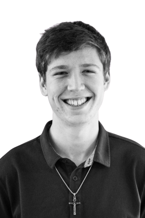 Black and white portrait of a young man smiling, wearing a patterned collared shirt, with short dark hair, and a plain background.