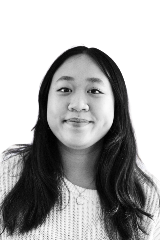 Black and white headshot of a young man smiling, with short, dark wavy hair, wearing a dark shirt and a chain necklace.