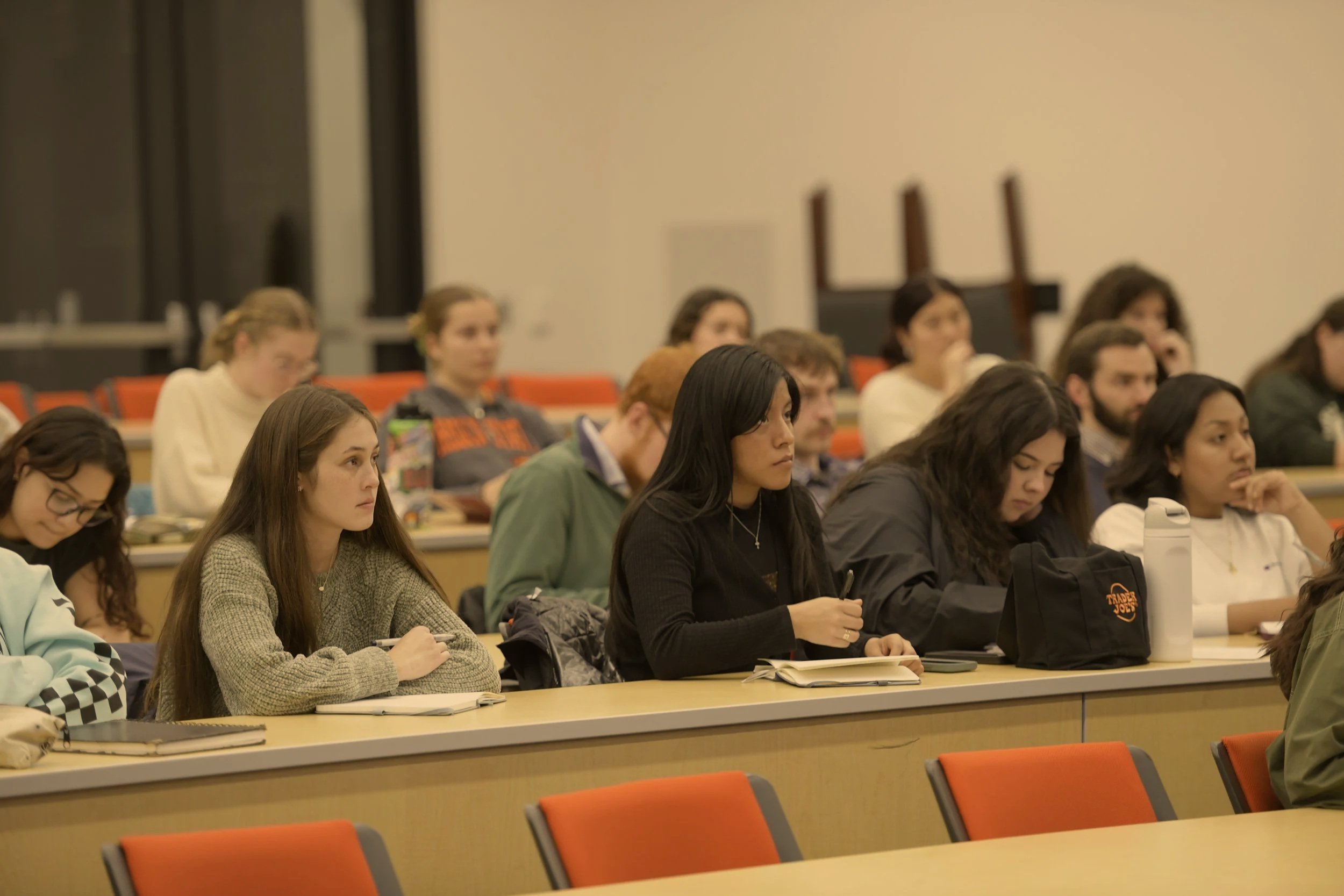 Students sitting at desks in a lecture hall, listening to a lecture.