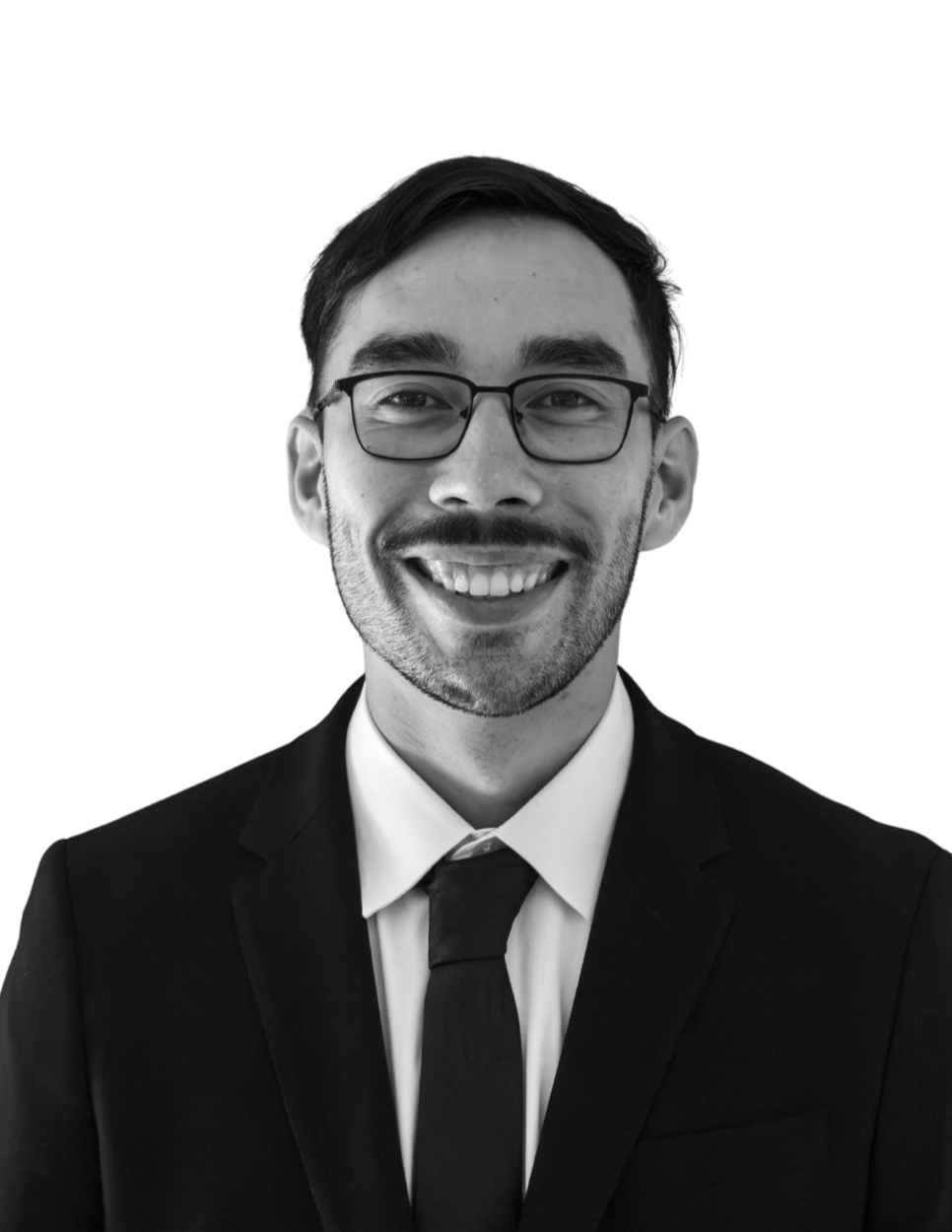 A black-and-white photo of a smiling man with curly hair, wearing a suit, dress shirt, and tie, standing against a plain background.