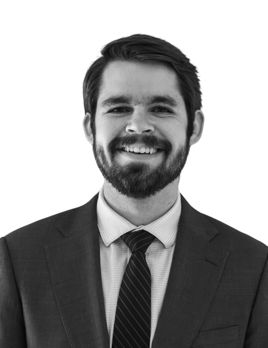 Black and white photo of a man with curly hair and a beard, smiling, dressed in a suit and tie, standing against a plain background.