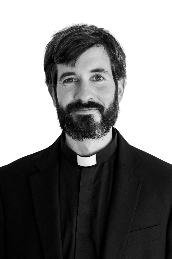 Portrait of a smiling priest with a beard, wearing a a dark suit.