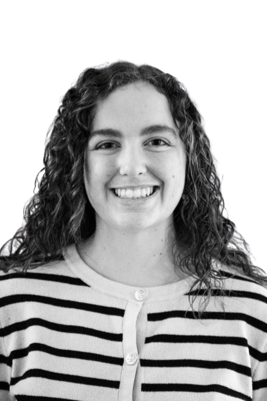 Black and white portrait of a young woman with long dark hair, smiling, wearing a collared sweater and layered necklaces, against a plain background.