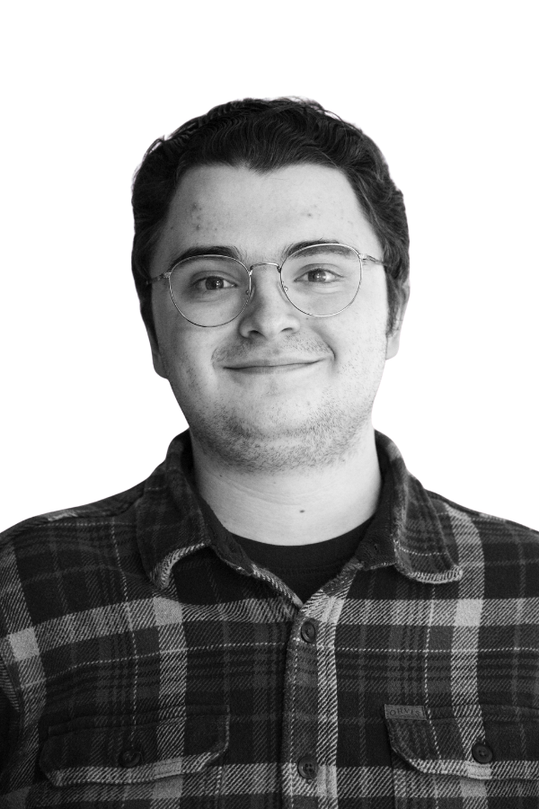 A black and white portrait of a young woman with long wavy hair, smiling and showing teeth, against a plain background.