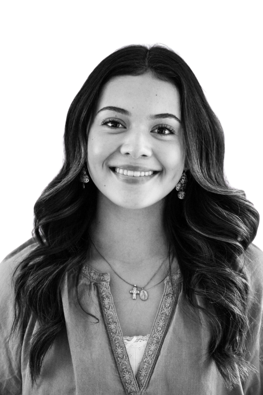 Black and white portrait of a young woman with long curly hair, hoop earrings, a nose ring, and a gentle smile, against a plain background.