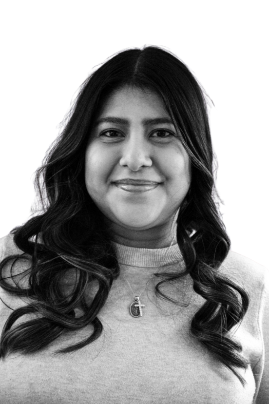 A black and white portrait of a woman with long wavy dark hair, wearing hoop earrings, a necklace, and a white top with a Calvin Klein Jeans logo.