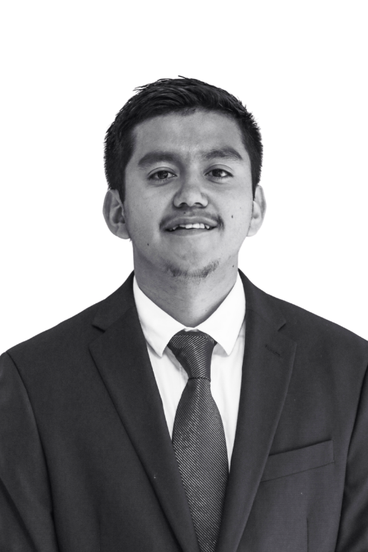 A black and white photo of a young man in a suit and tie, smiling, against a plain background.