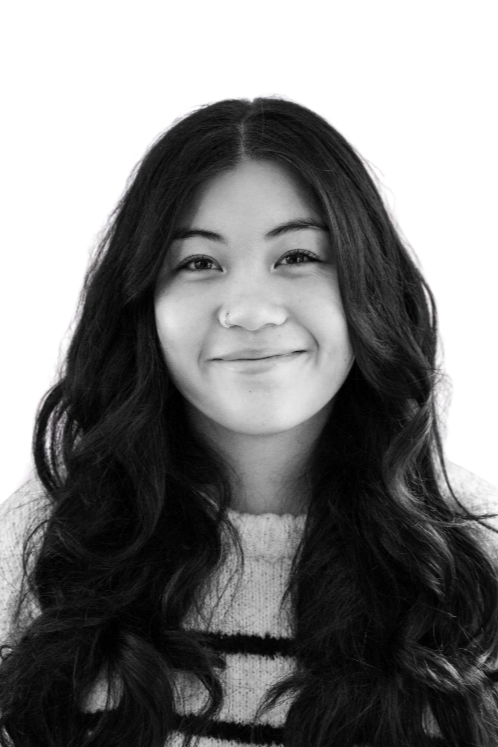 Black and white portrait of a smiling young woman with shoulder-length hair and light eyes, wearing a patterned sweater and a pearl necklace.