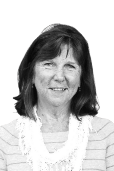 Black and white photo of a woman with shoulder-length dark hair, wearing a striped top and a lace scarf, standing in front of a brick wall.