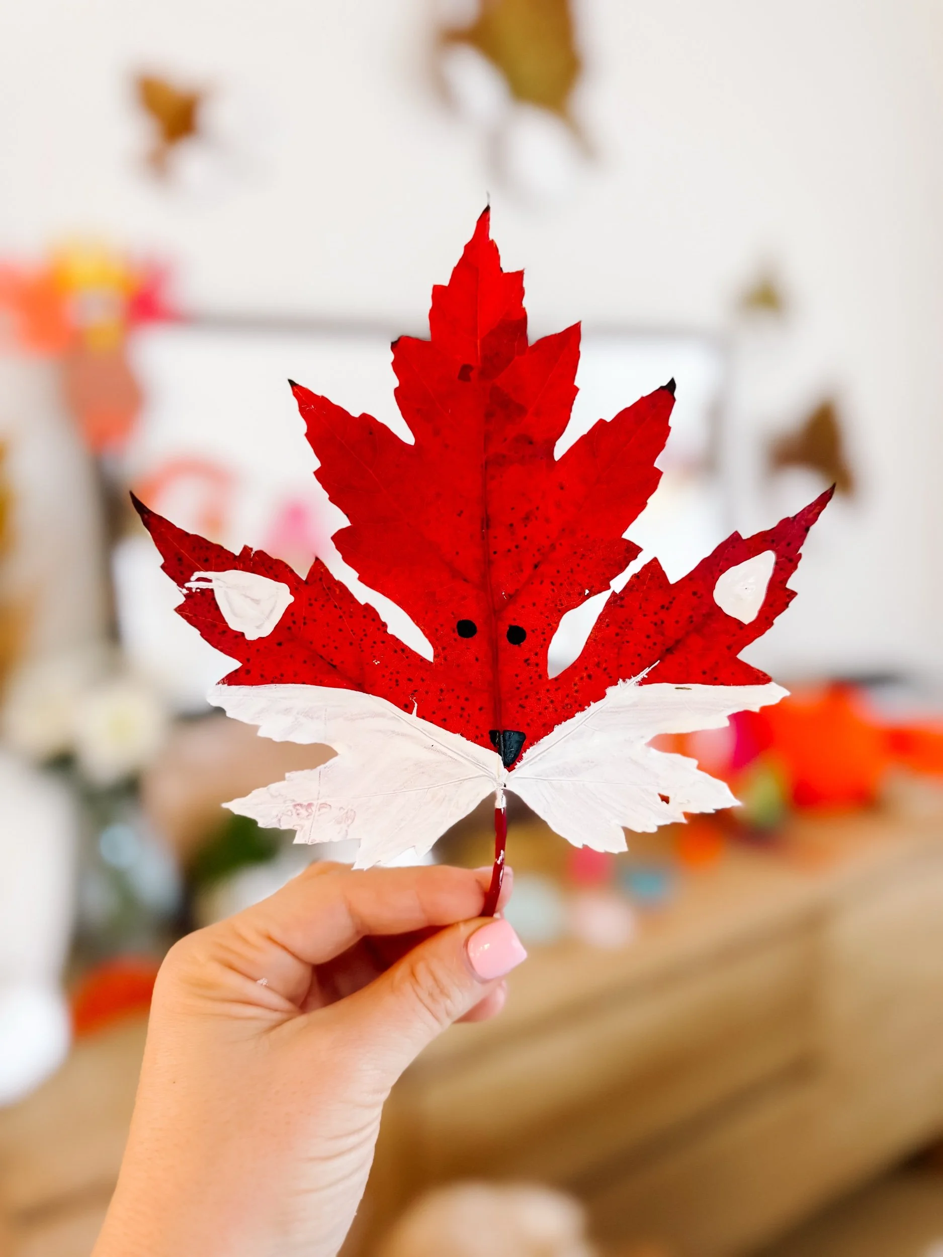 Finished red maple leaf fox craft with white painted cheeks, black eyes, and a black nose.