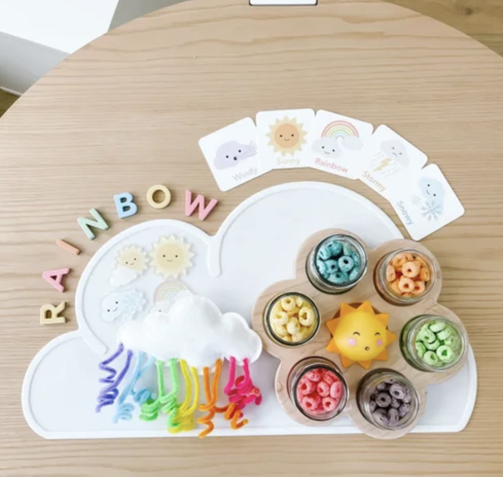 Rainbow cloud craft setup with Fruit Loops sorted by color, weather cards, pipe cleaners, and cloud tray.