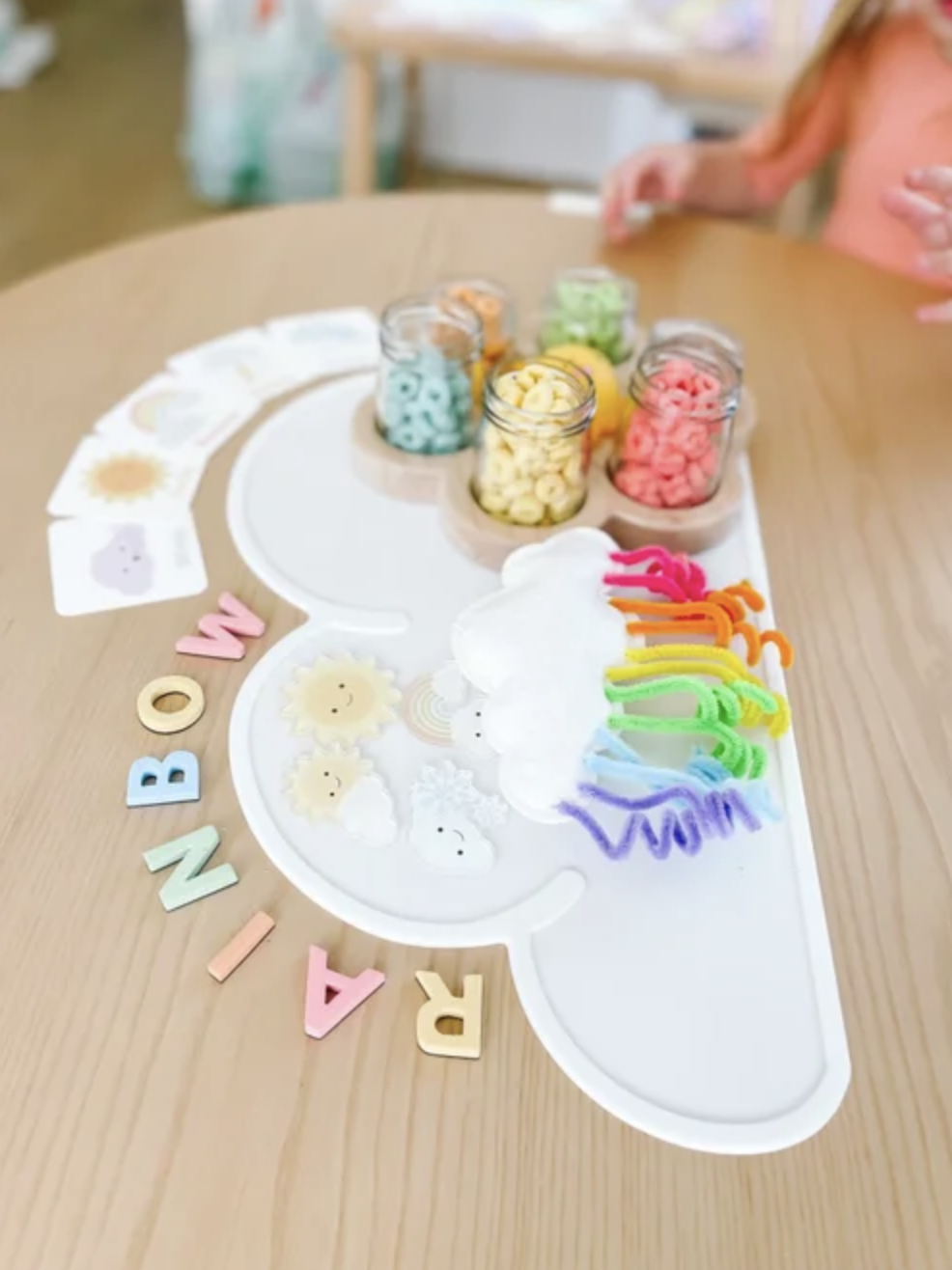 Rainbow pipe cleaners and colorful Fruit Loops arranged on a cloud tray for a preschool craft.