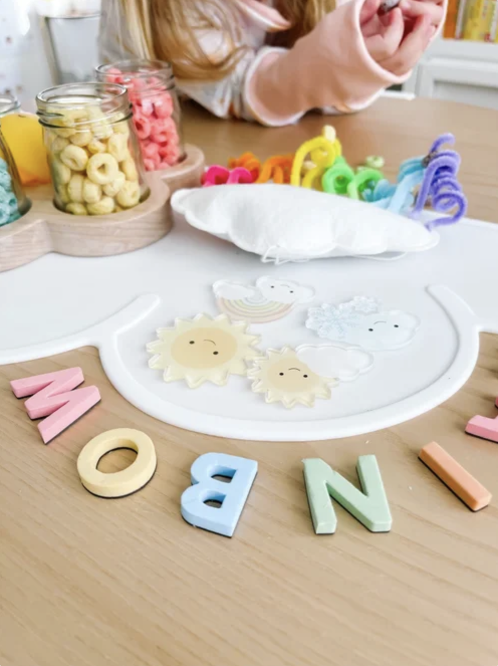 Close-up of rainbow threading activity with pipe cleaners, Fruit Loops, weather pieces, and letter tiles.