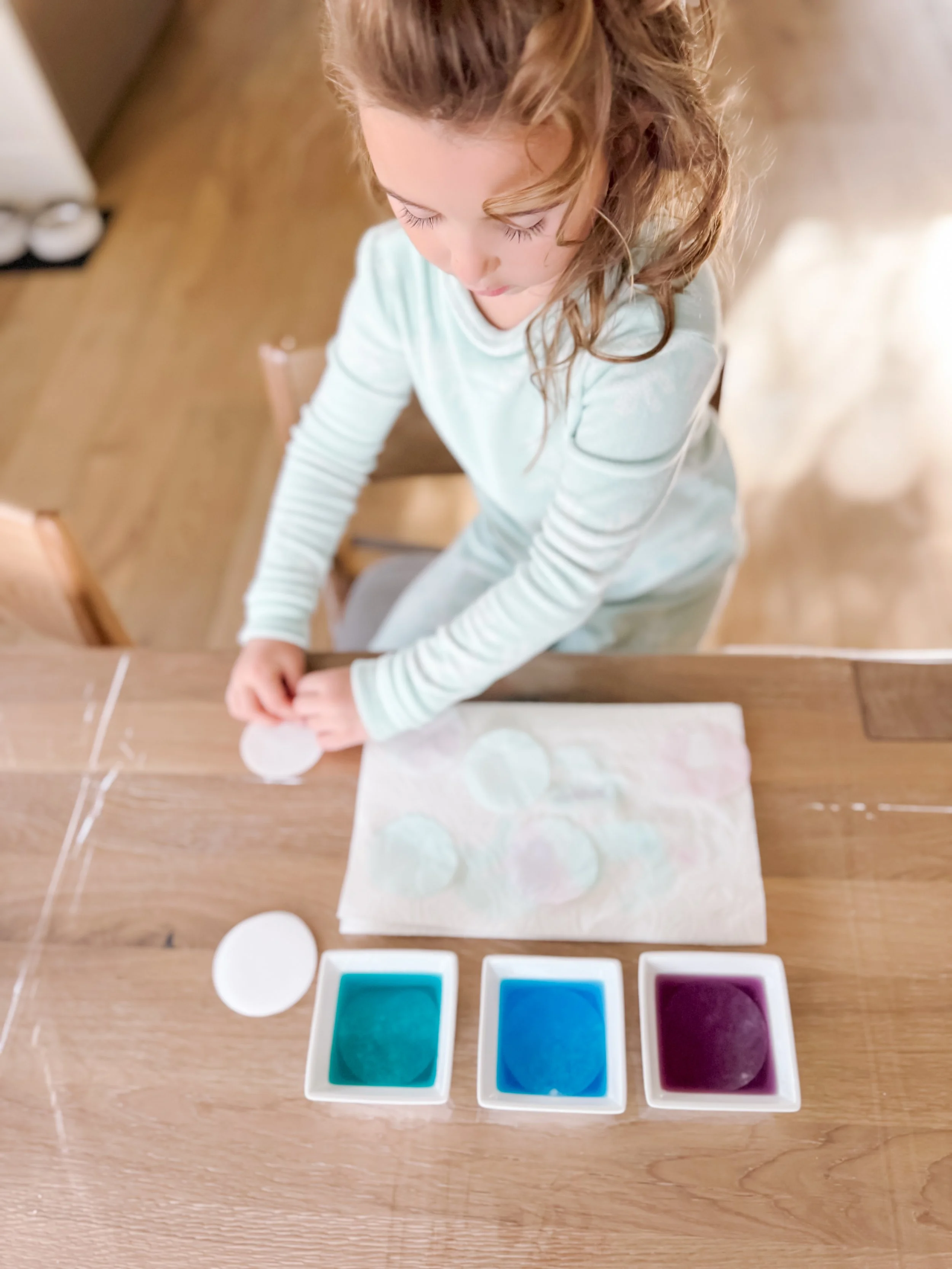  Colored coffee filters drying on a tray after dipping, dripping, and spraying with food coloring for rainbow paper flower craft. 