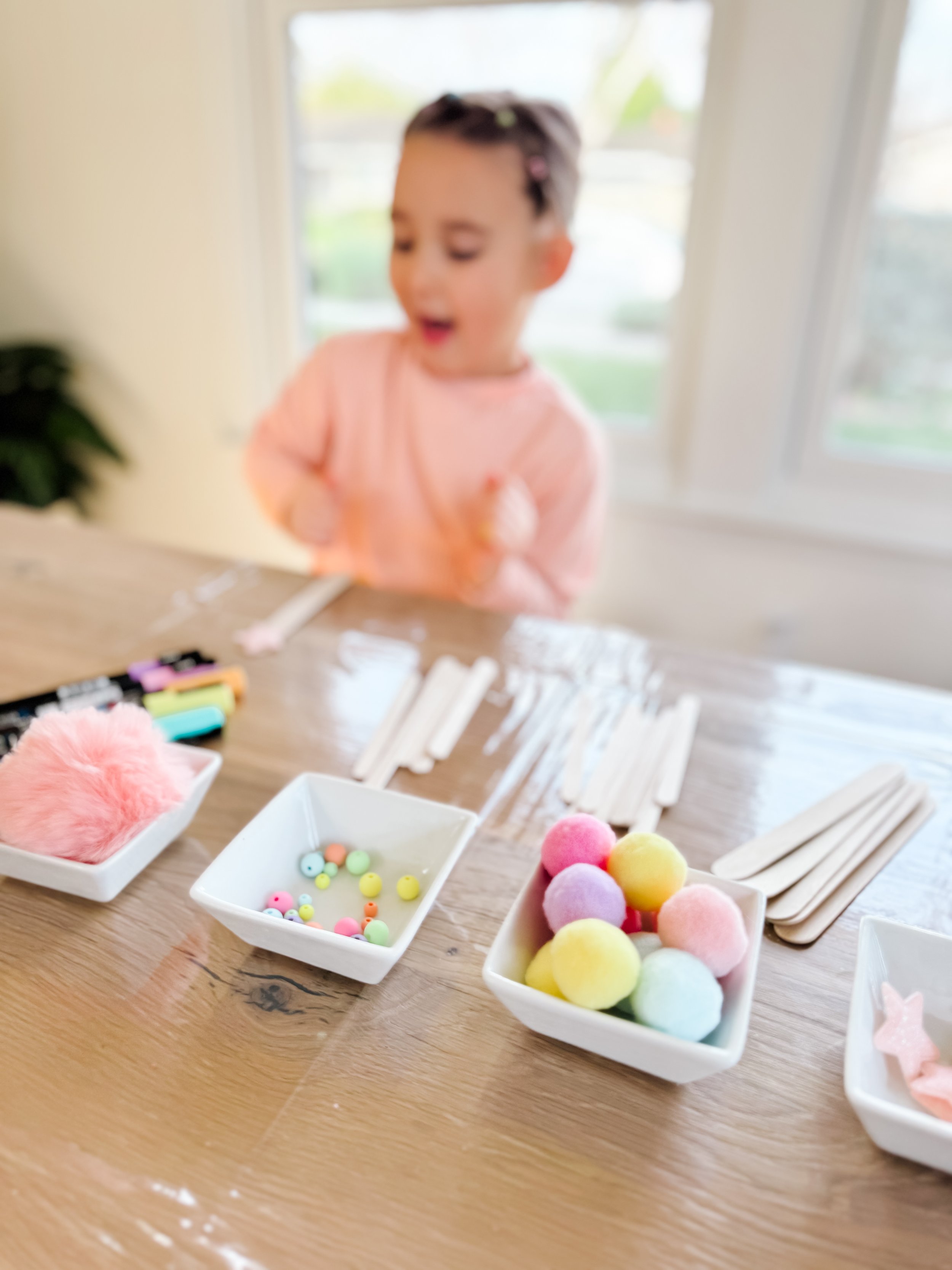 Pastel craft supplies for a dreamcatcher-inspired weaving activity, including wooden sticks, yarn, beads, pom-poms and stars.