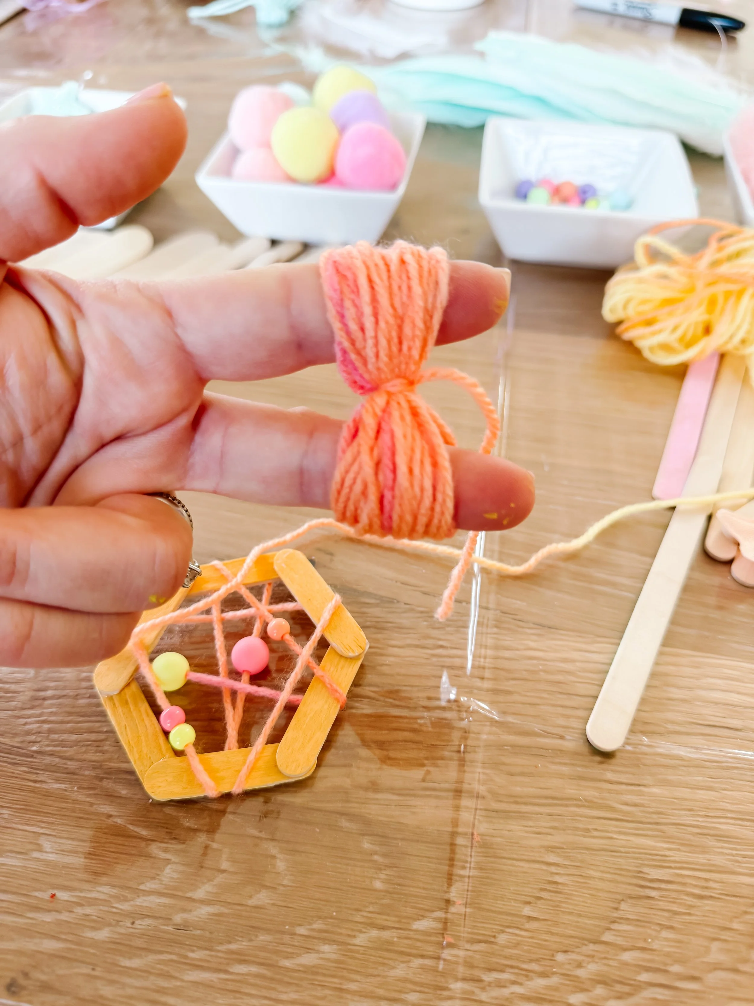 Hand holding a small bundle of coral yarn tied in the middle to begin making a tassel.