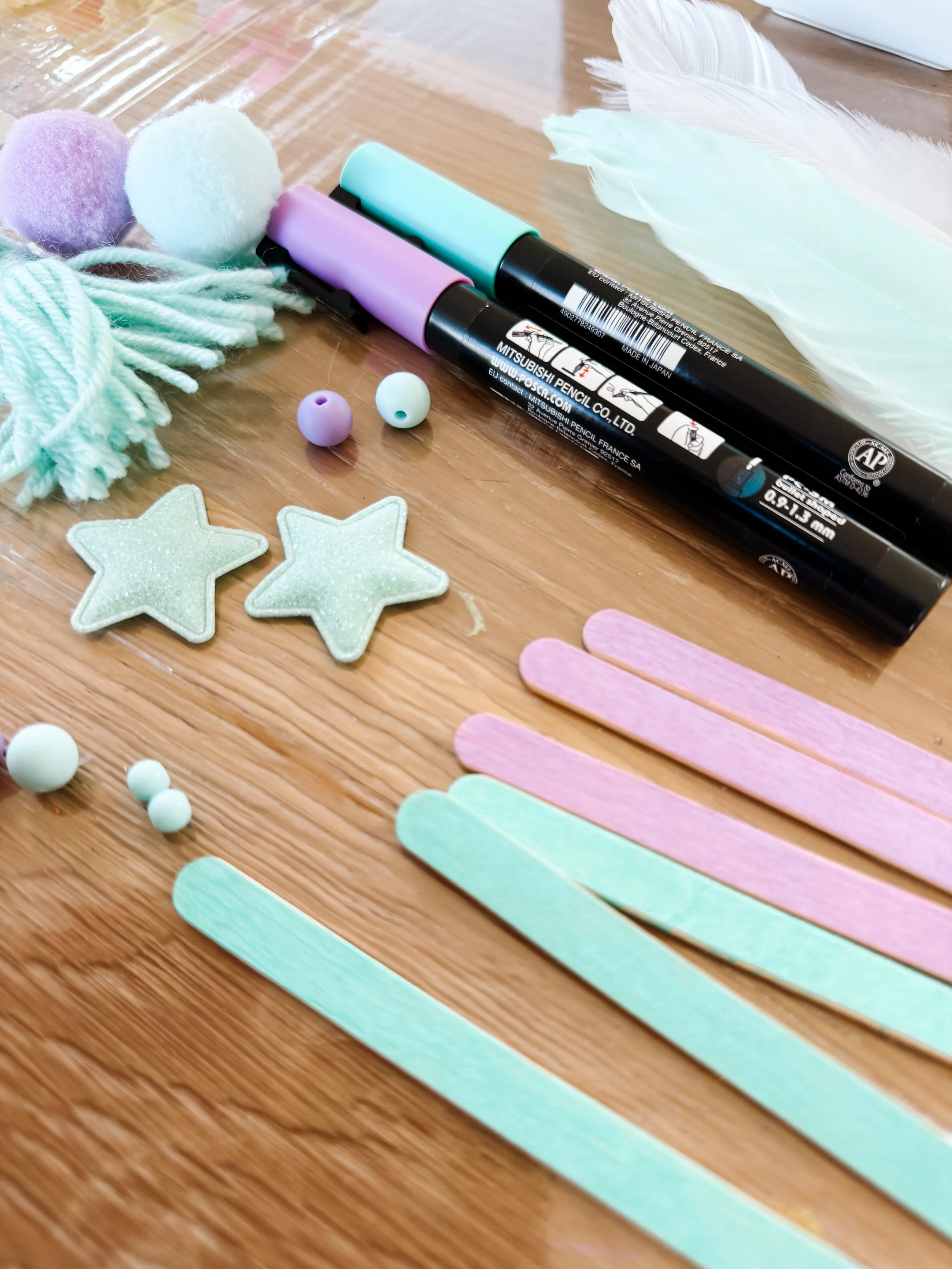 Pastel craft sticks, mint feathers, stars, beads, paint markers, pom-poms and tassel supplies.