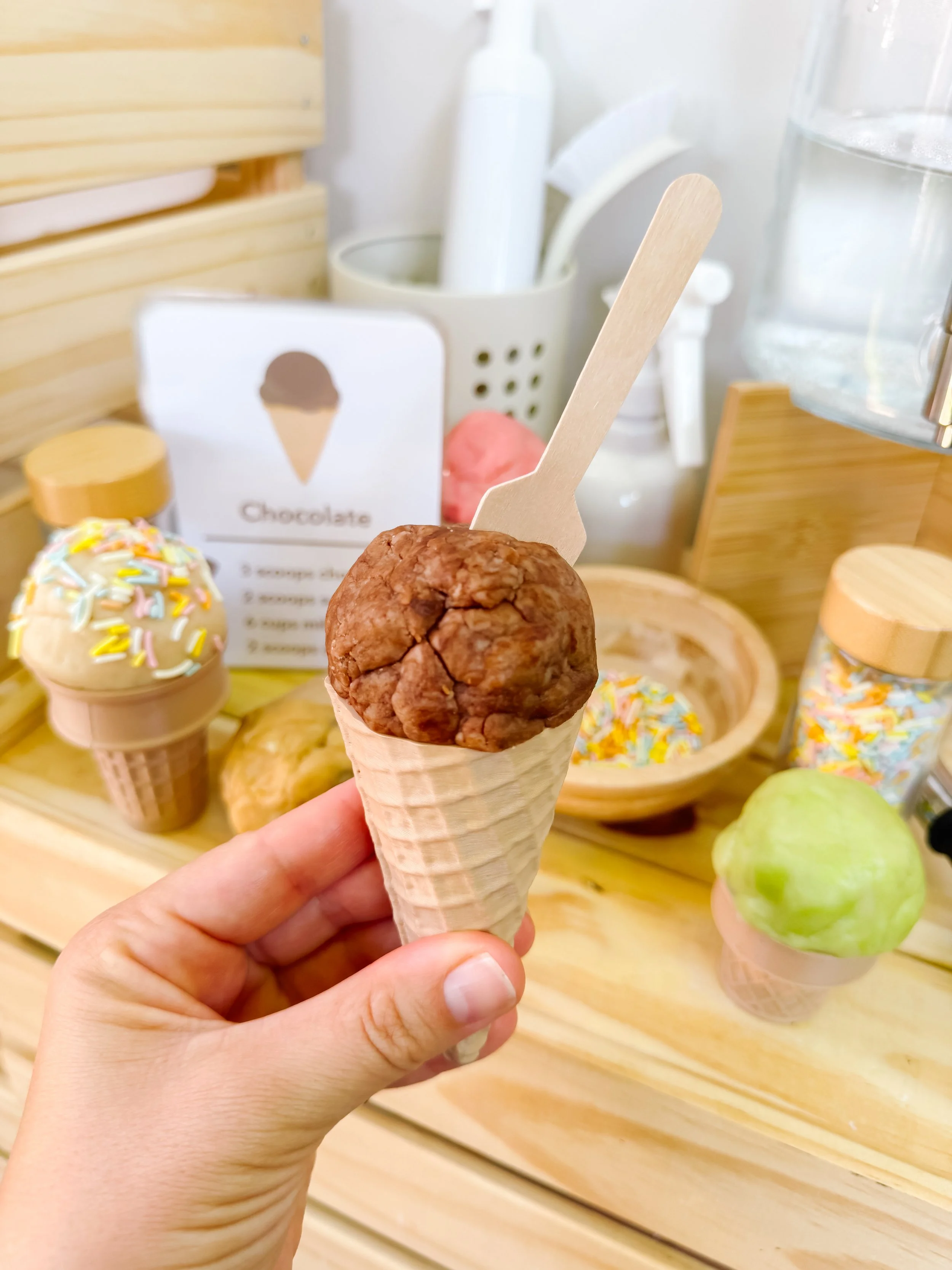 Pretend chocolate ice cream cone in a mud kitchen setup with recipe cards and play accessories.
