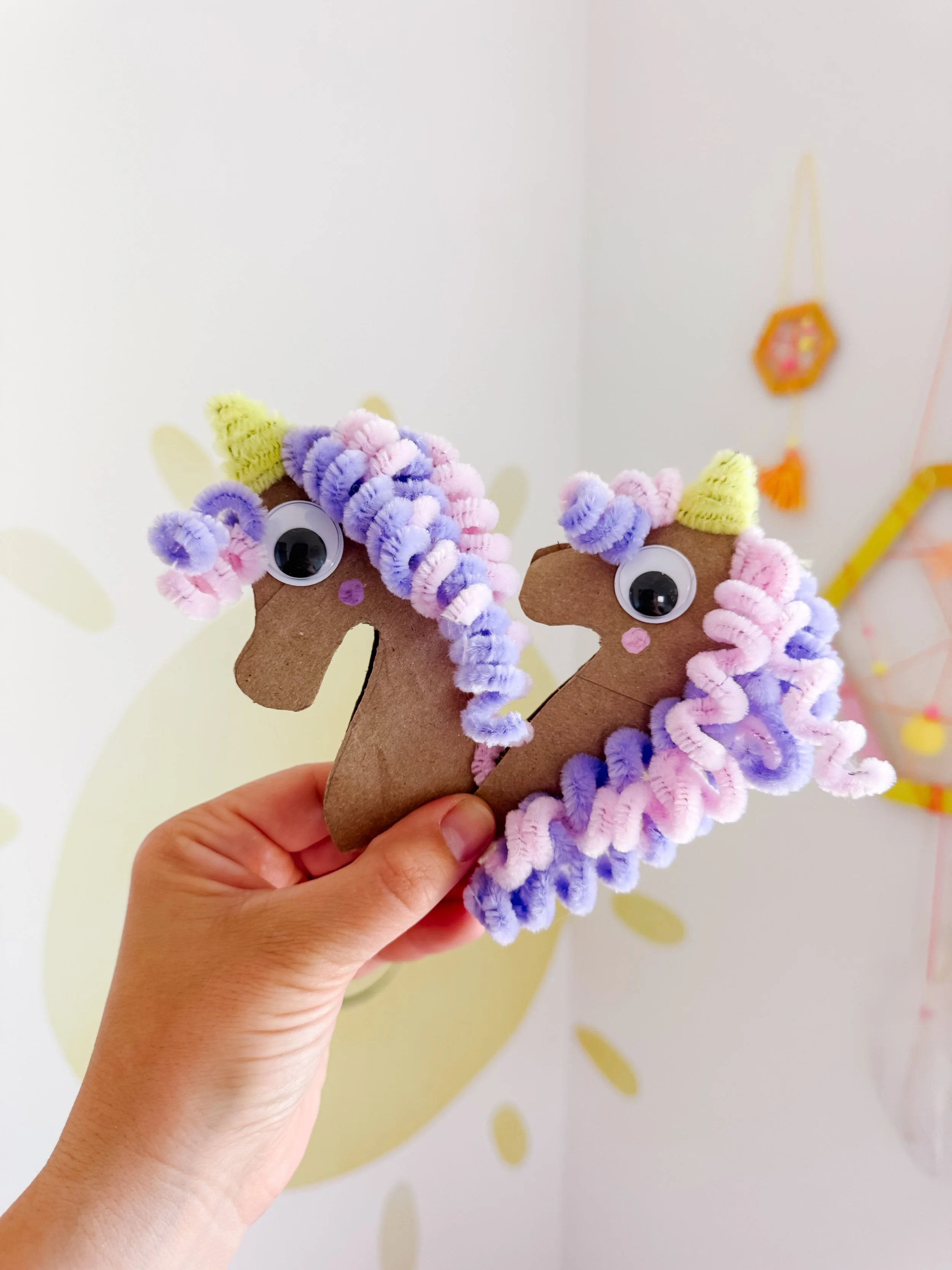 Child holding two pastel toilet roll unicorn crafts for imaginative play.