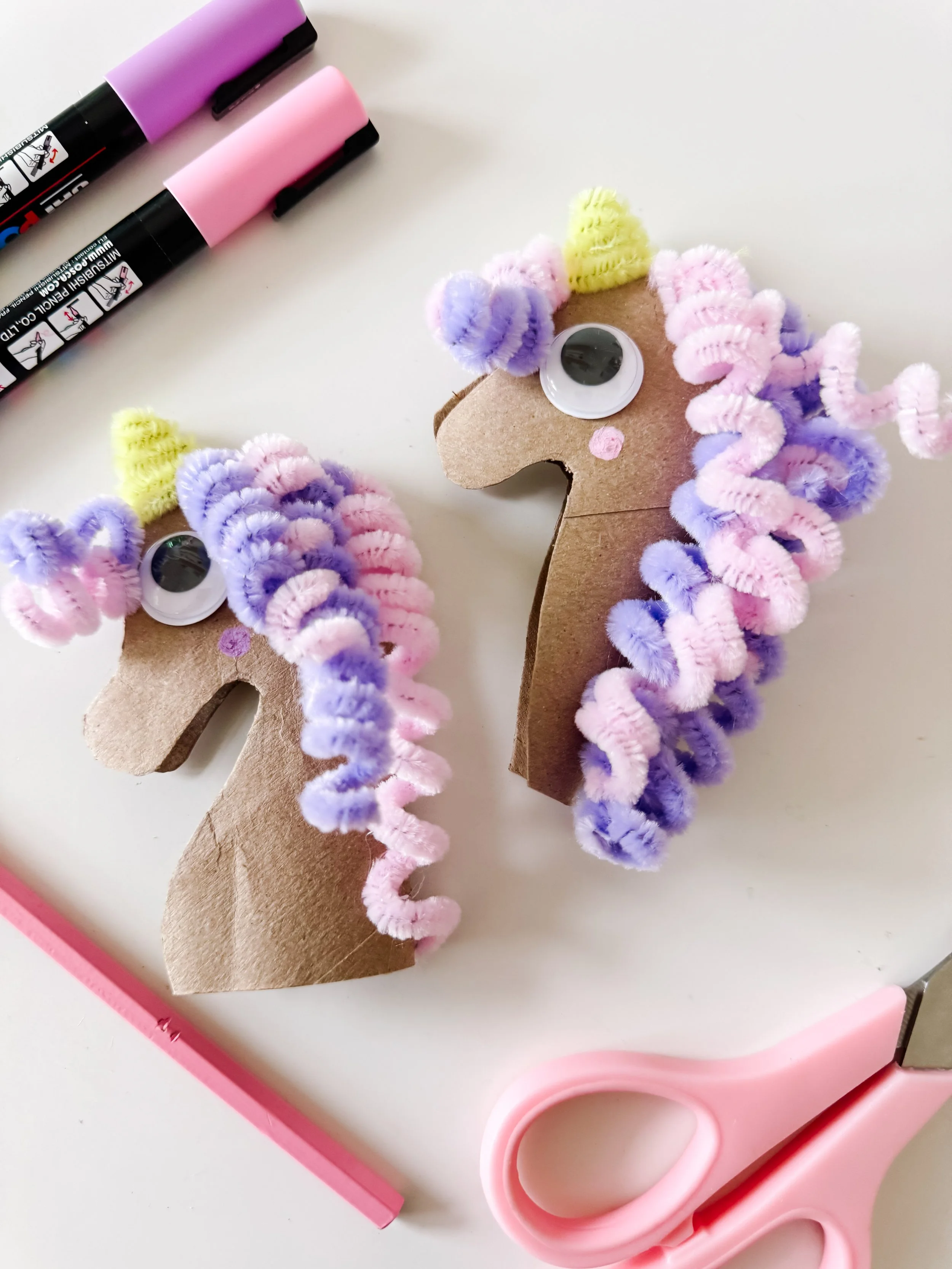 Two completed toilet roll unicorn crafts with curled pastel pipe cleaner manes.