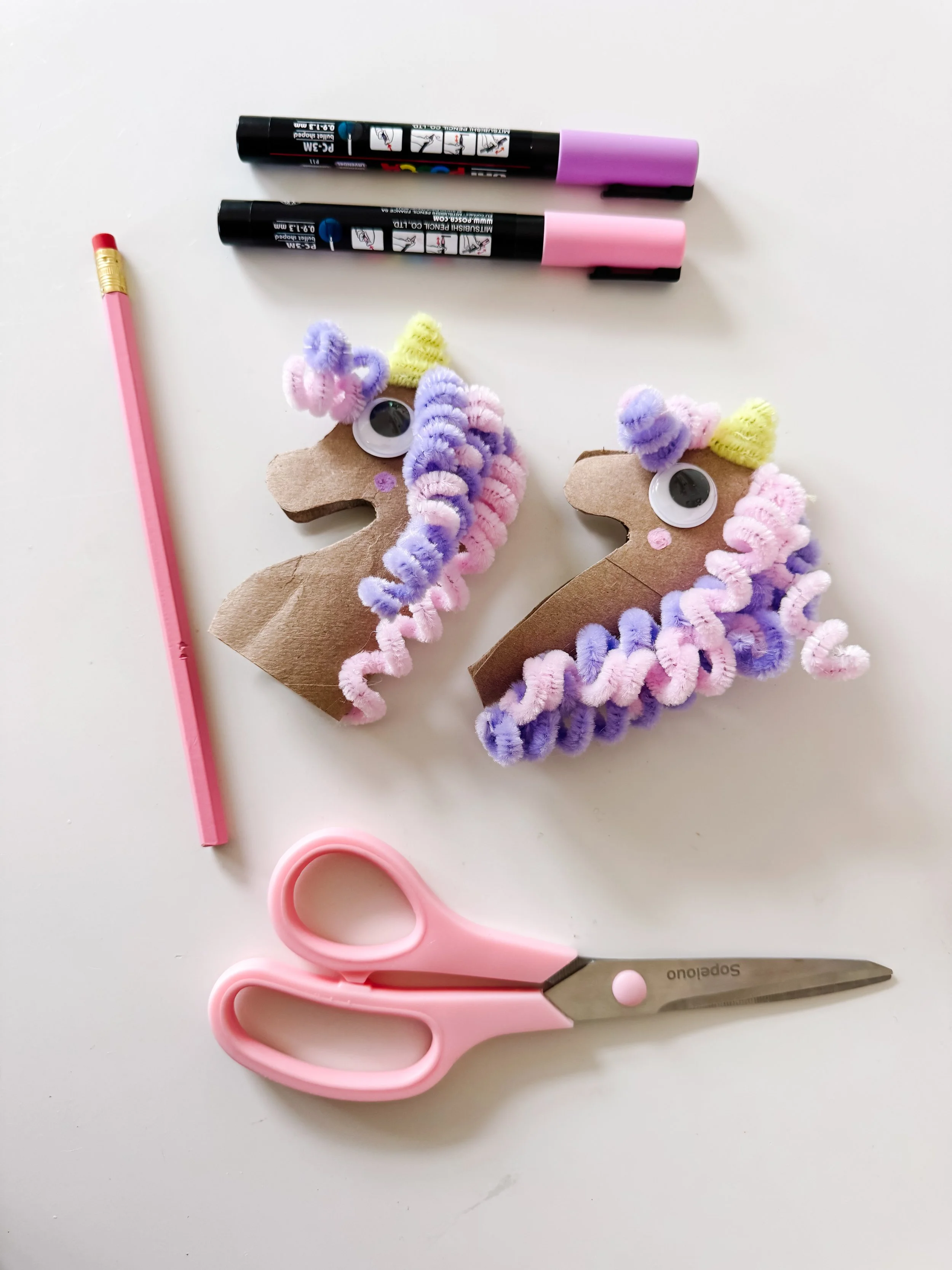 Finished toilet roll unicorn crafts with pastel pipe cleaner manes, yellow horns, and craft supplies.