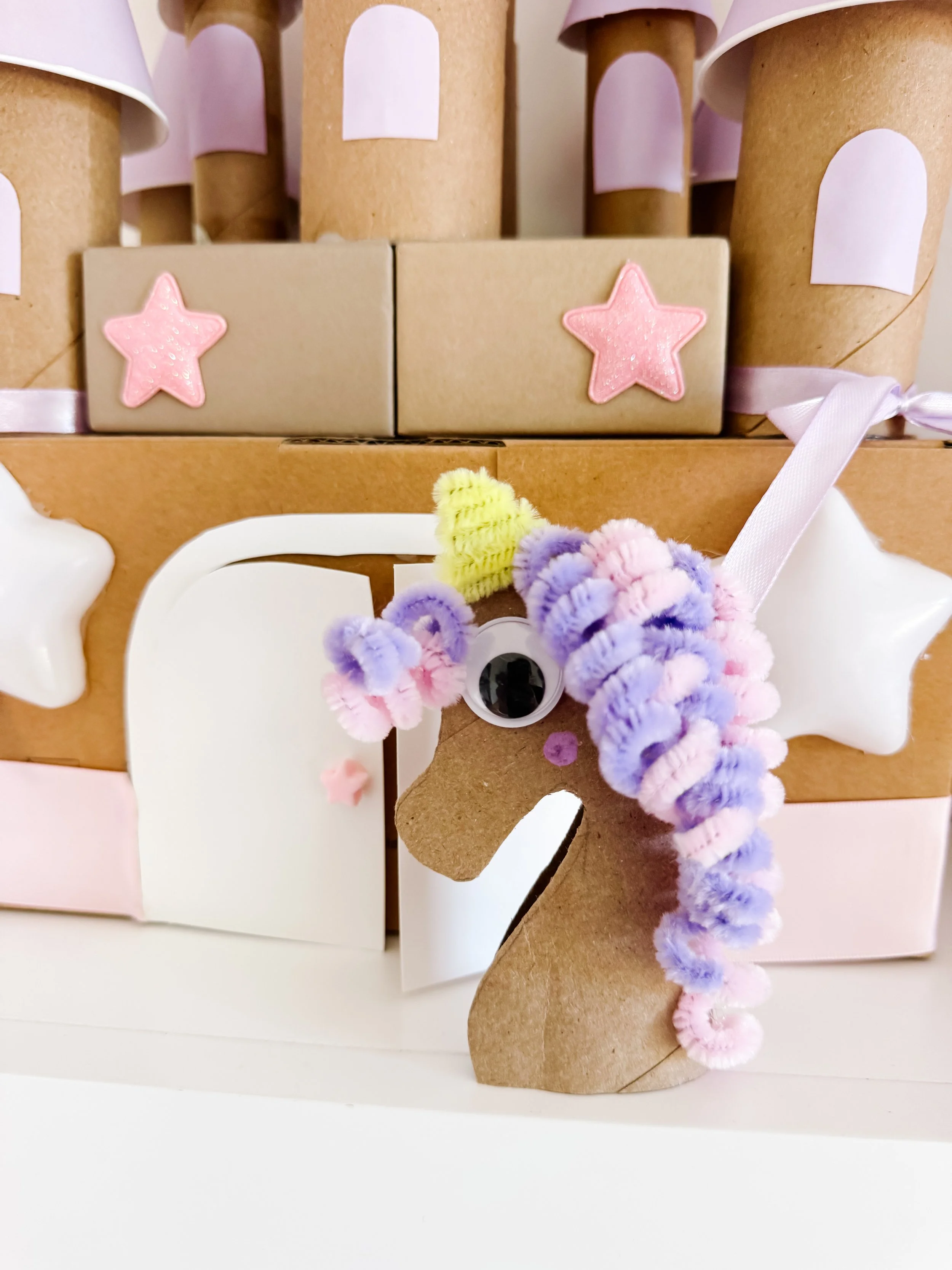 Toilet roll unicorn craft in front of a DIY cardboard castle.