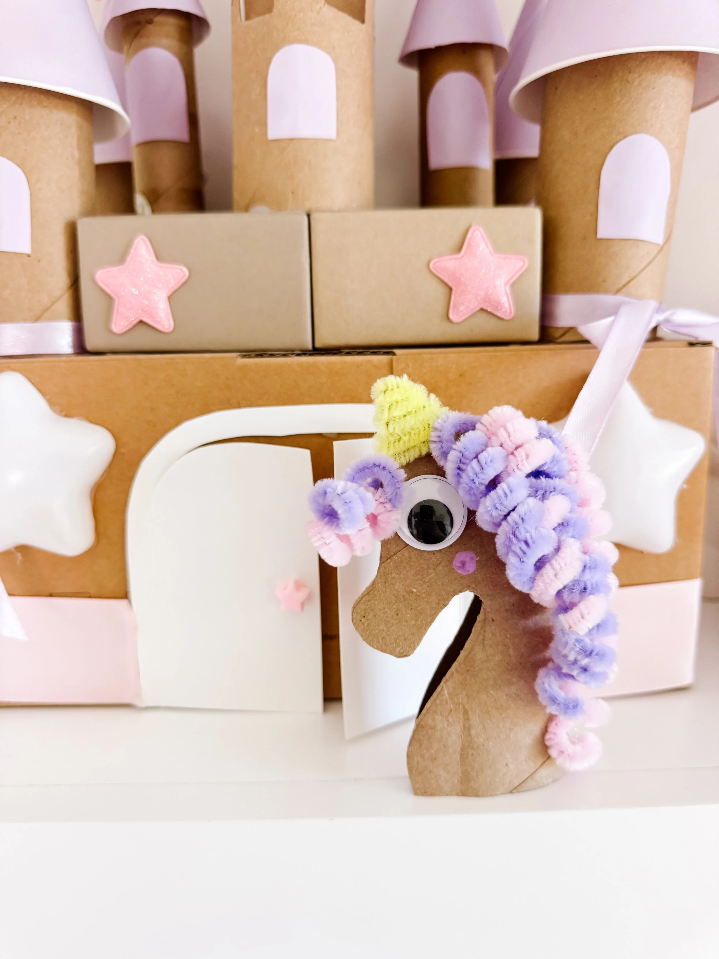 Toilet roll unicorn craft standing in front of a cardboard castle.