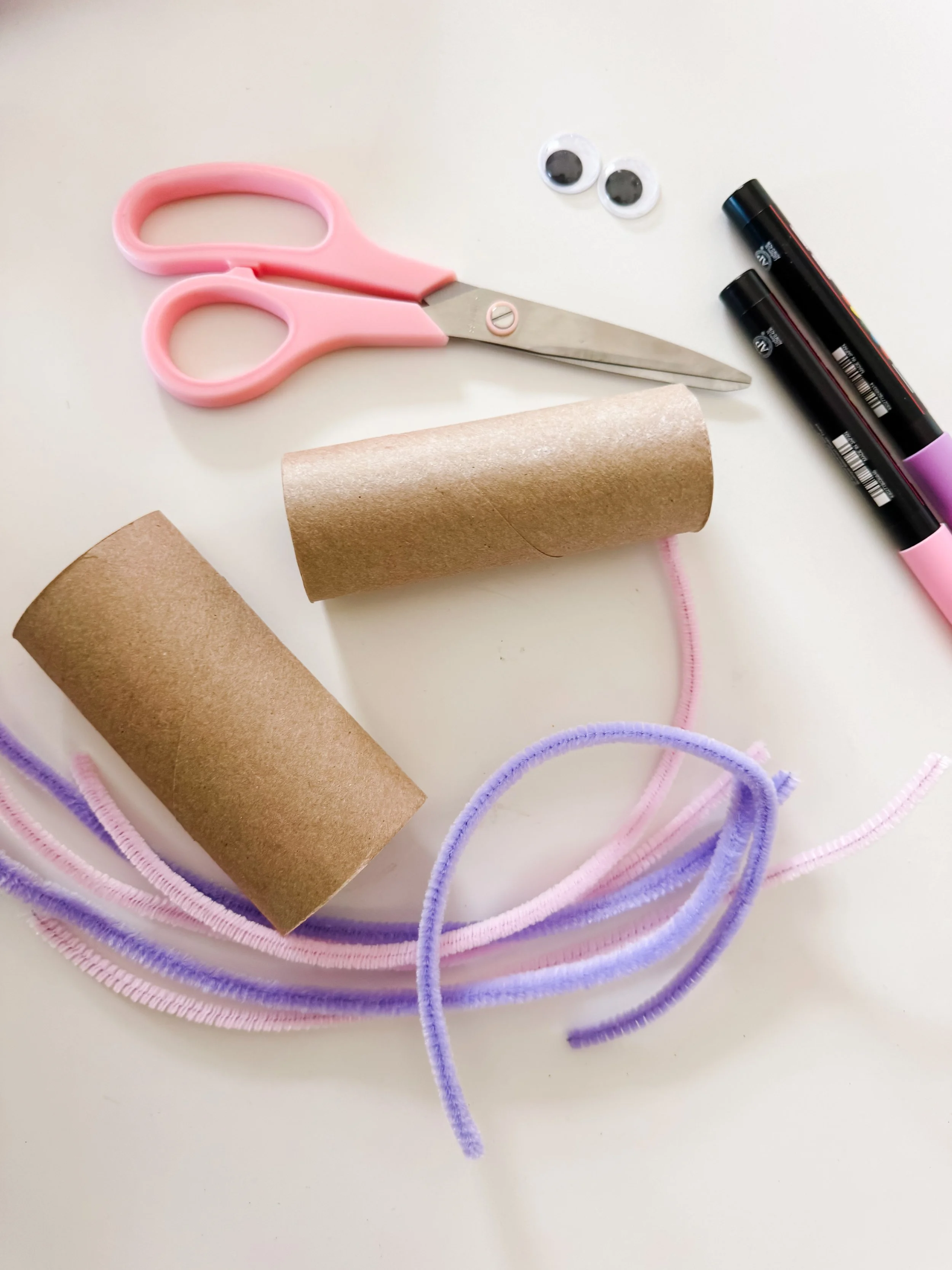 Supplies for toilet roll unicorn craft including cardboard tubes, pipe cleaners, scissors, markers, and googly eyes.