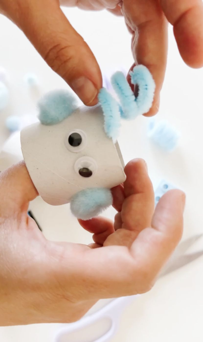 Adding googly eyes and curled blue pipe cleaner antennae to the cardboard robot head.