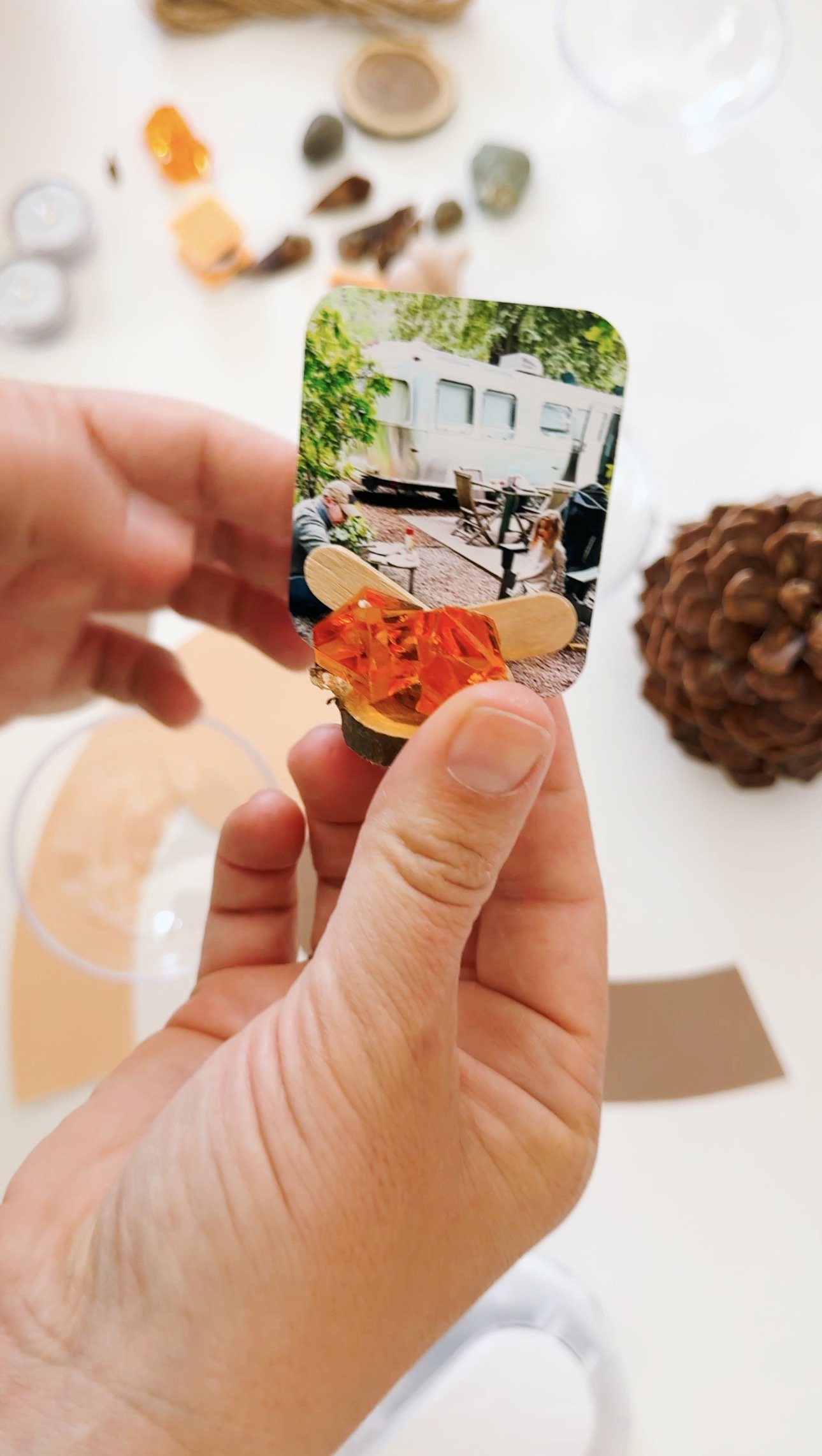 Creating a miniature camping scene with a family photo, orange gems, wooden pieces, and a plastic s'more.