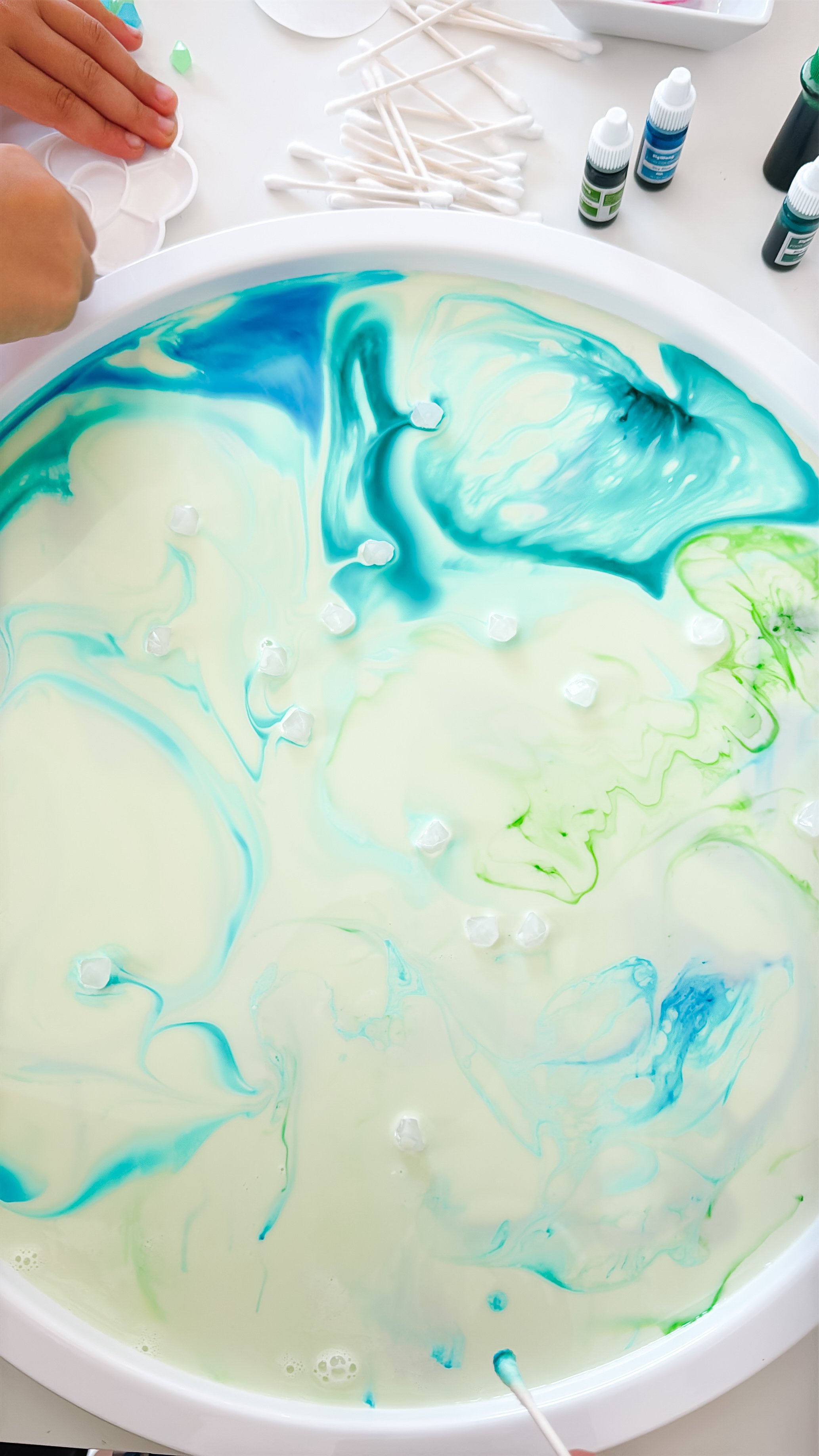 Blue, turquoise, and green food coloring beginning to spread across milk after contact with dish soap.