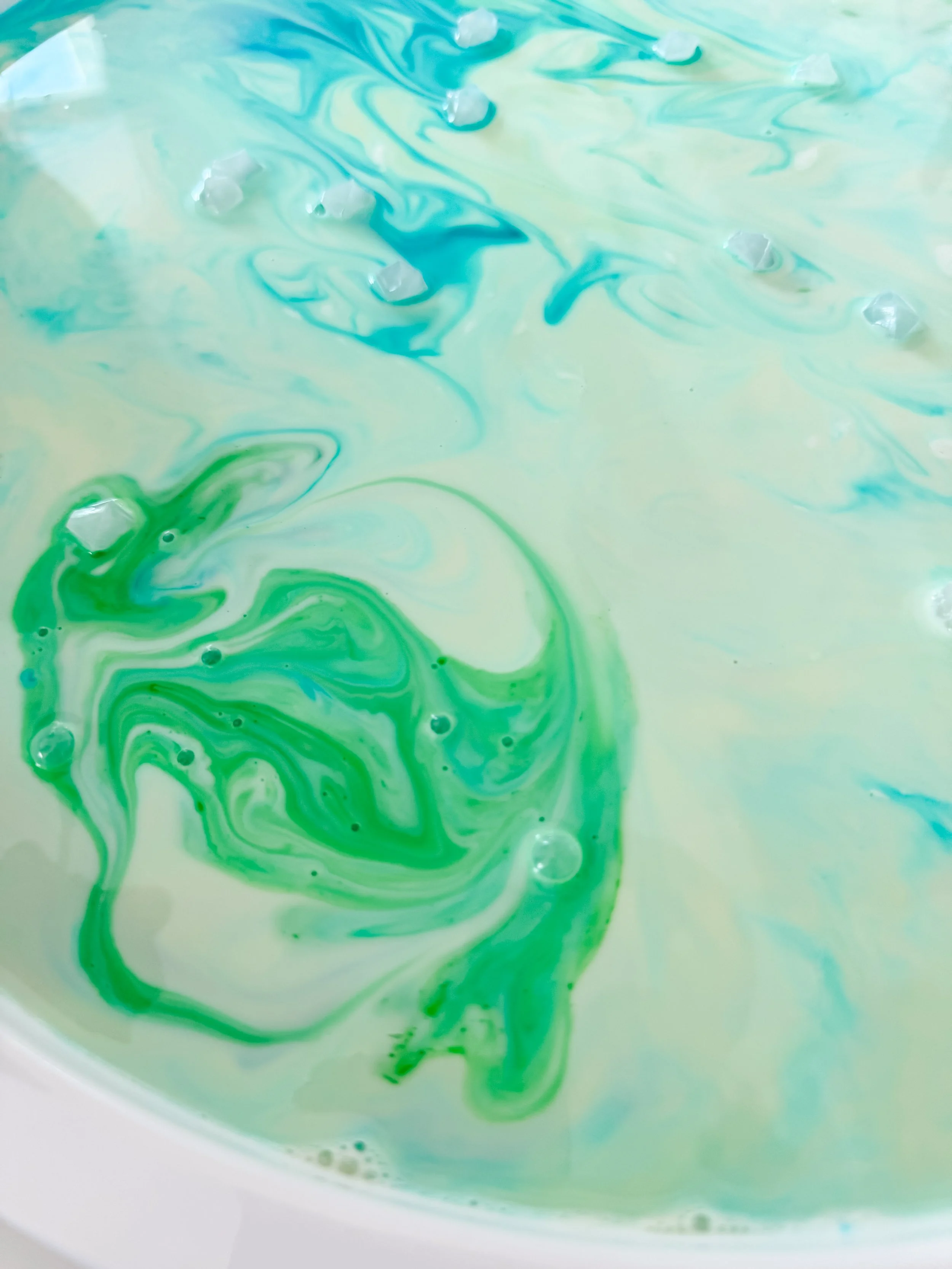 Green aurora-shaped pattern in milk surrounded by pale blue color and clear gems.