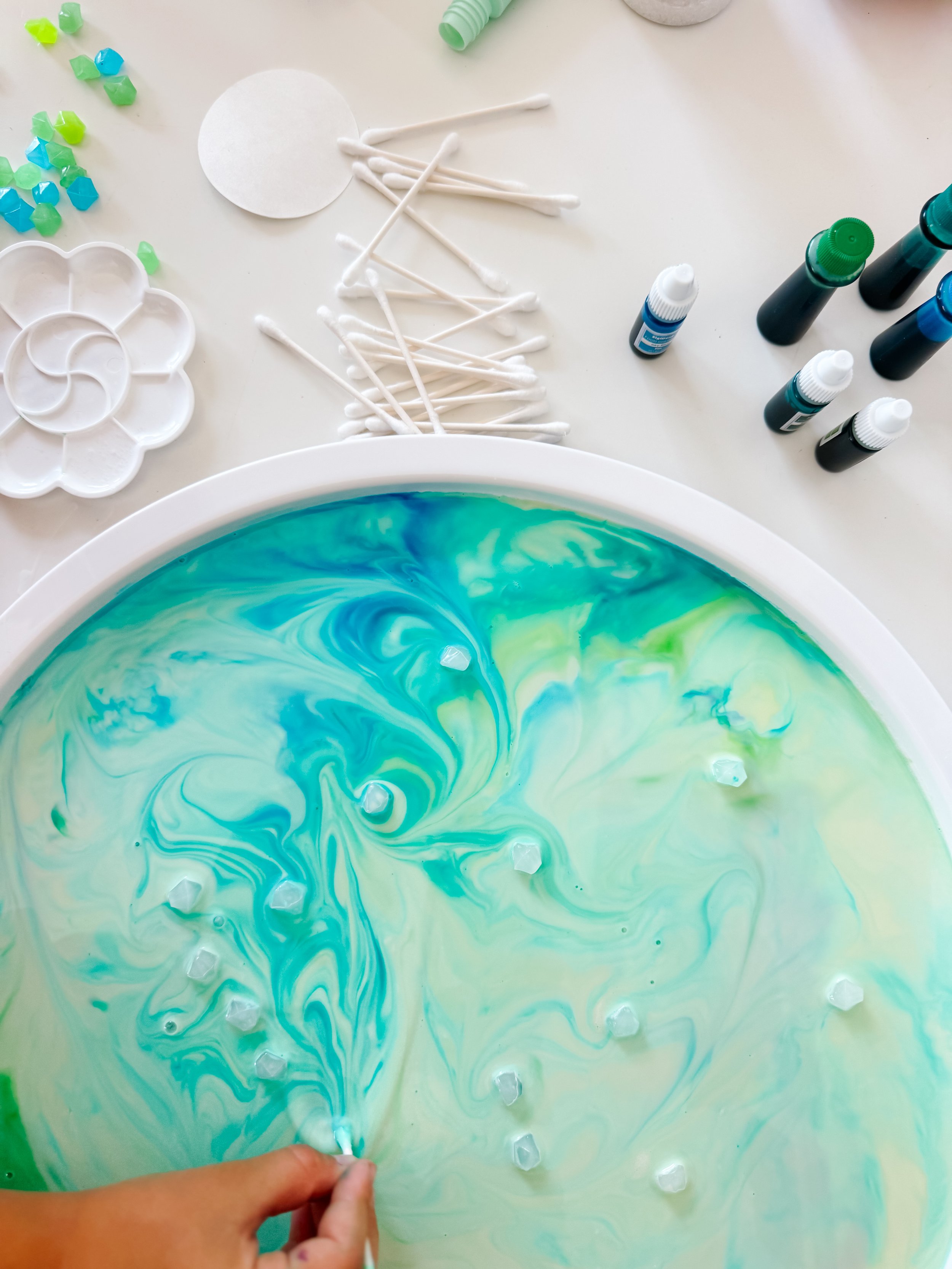 Child using a cotton swab to move turquoise and green colors through Northern Lights Magic Milk.