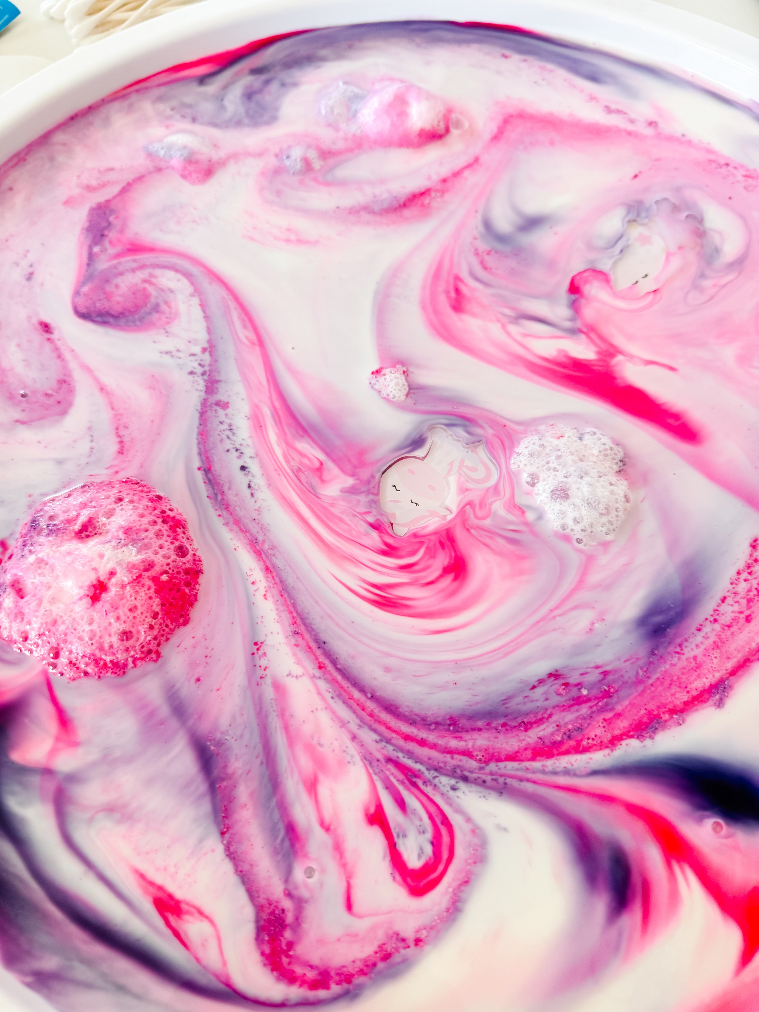 Two unicorn acrylic charms surrounded by pink and lavender Magic Milk swirls and bubbles.