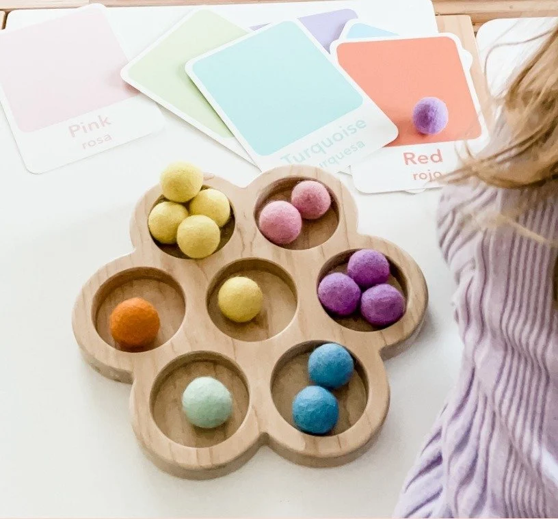 Felt balls sorted by color into a wooden flower tray beside color cards
