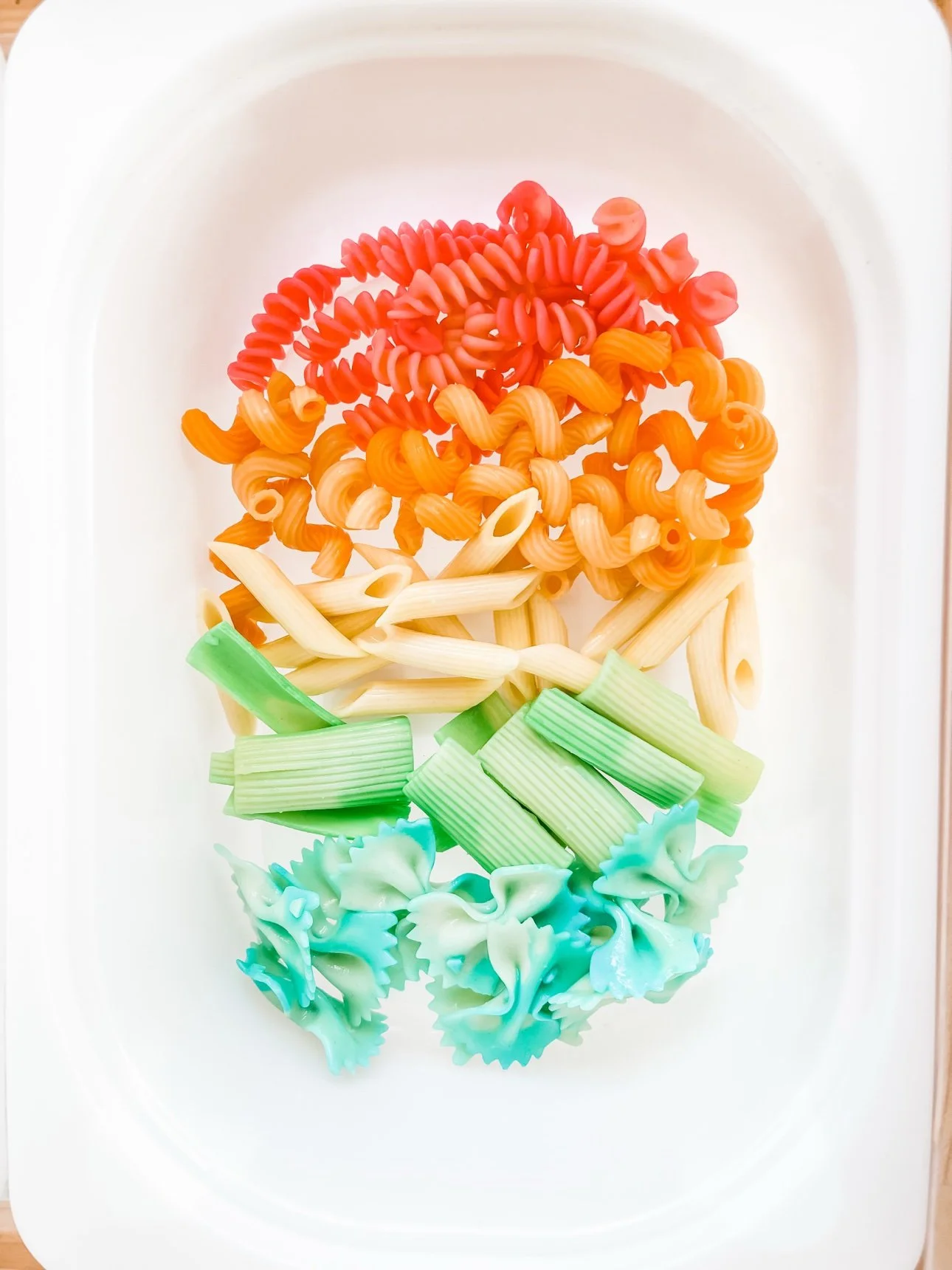 Rainbow pasta arranged in color bands in a sensory bin