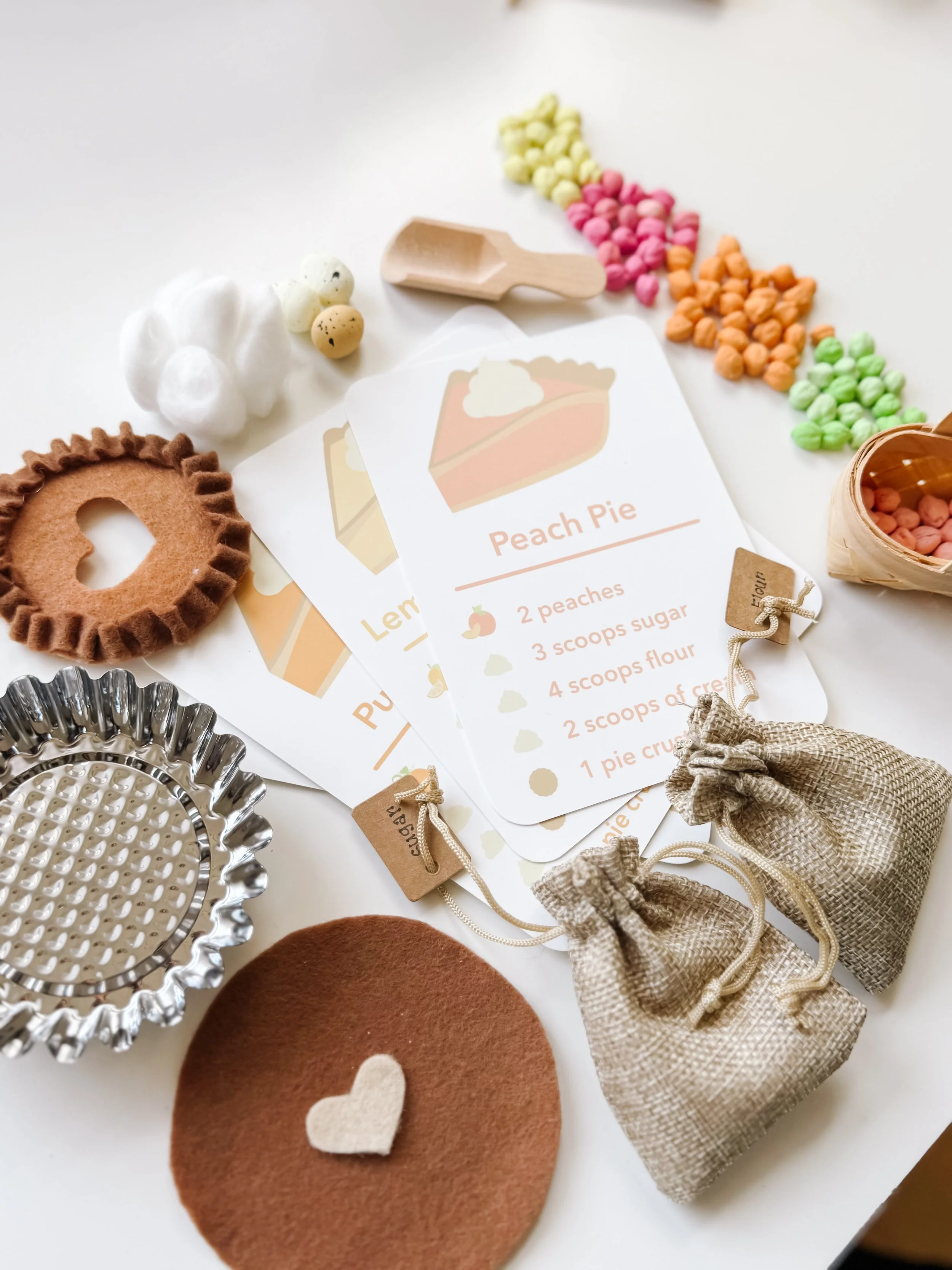 Pie Making Sensory Kit pieces arranged around the Peach Pie recipe card, including the metal pie tin, felt crust, burlap ingredient bags, and chickpea fillings