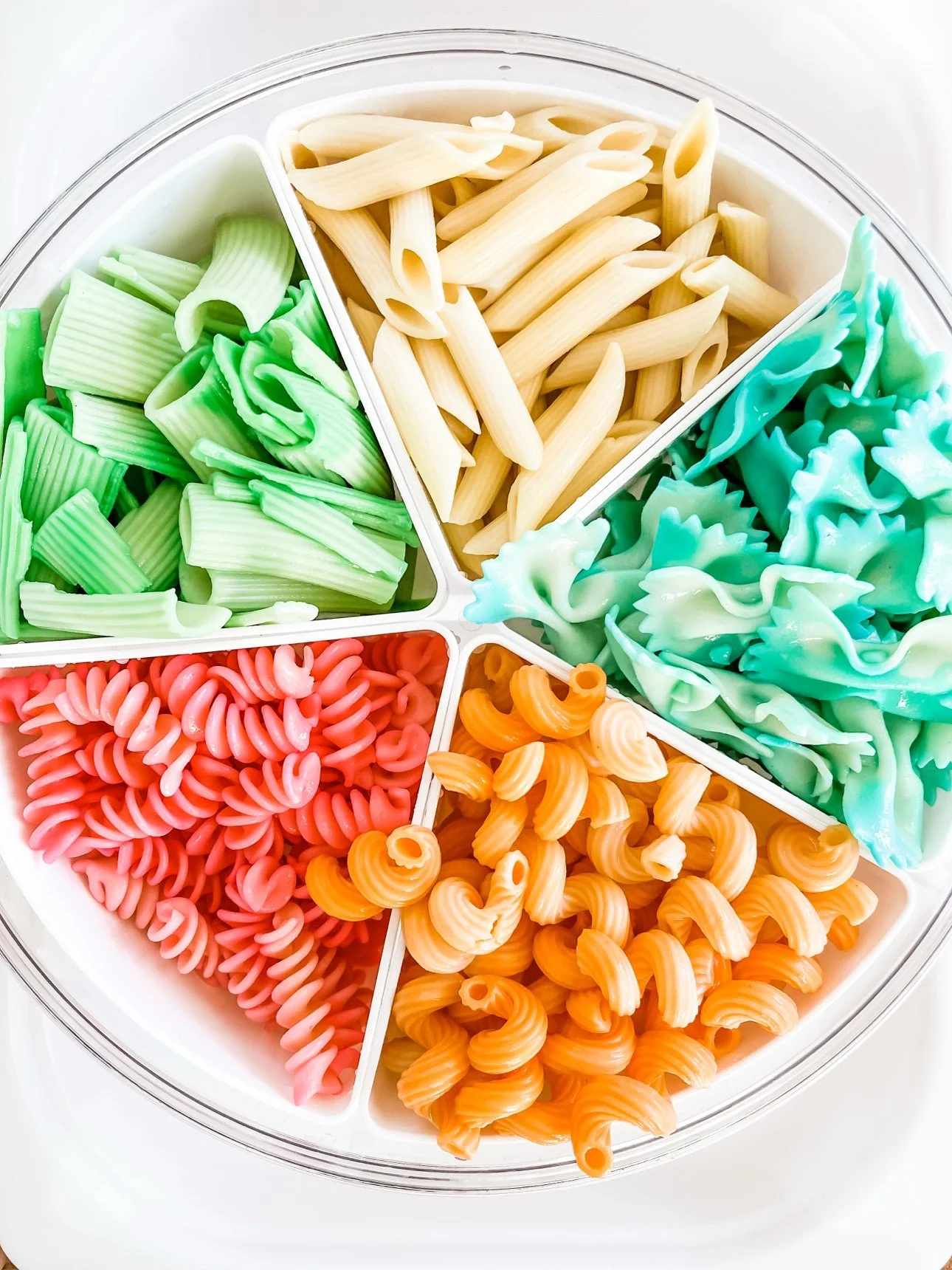 Dyed pasta shapes sorted by shape into the compartments of a divided tray