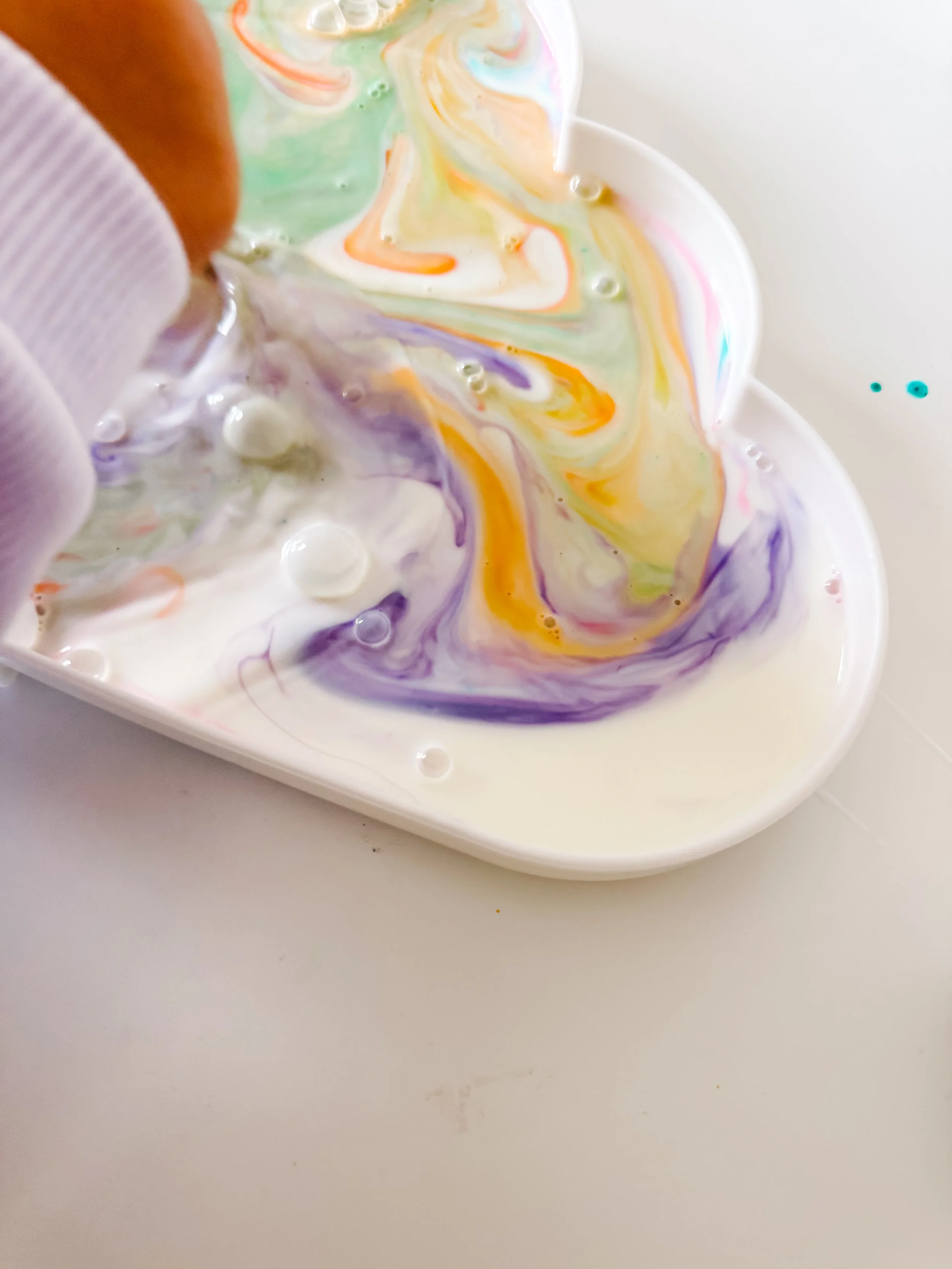 Rainbow milk experiment for kids with colorful food coloring swirling in a shallow dish of milk.
