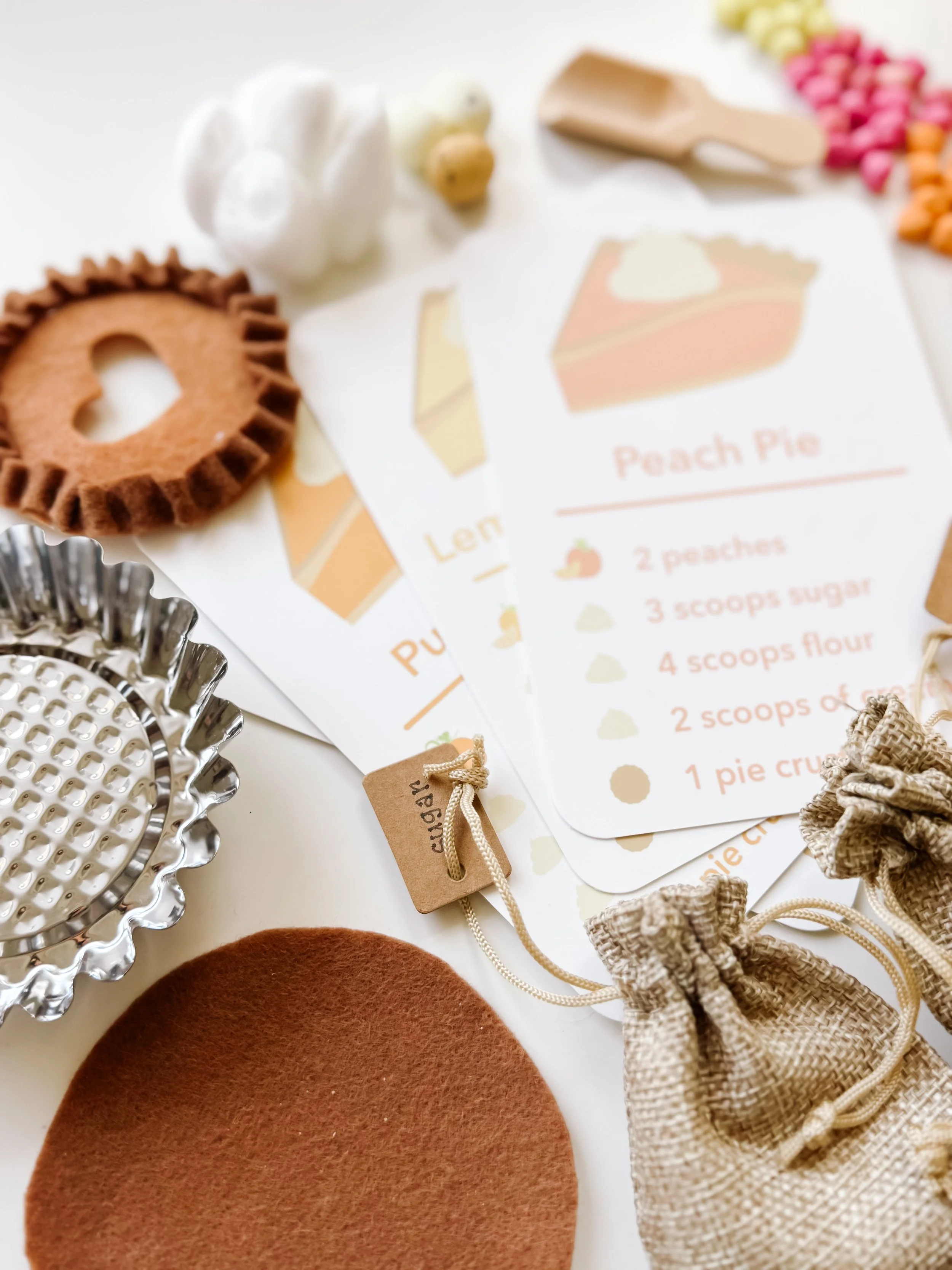 Pie recipe cards laid out with a felt pie crust, metal pie tin, wooden scoop, and burlap sugar bag