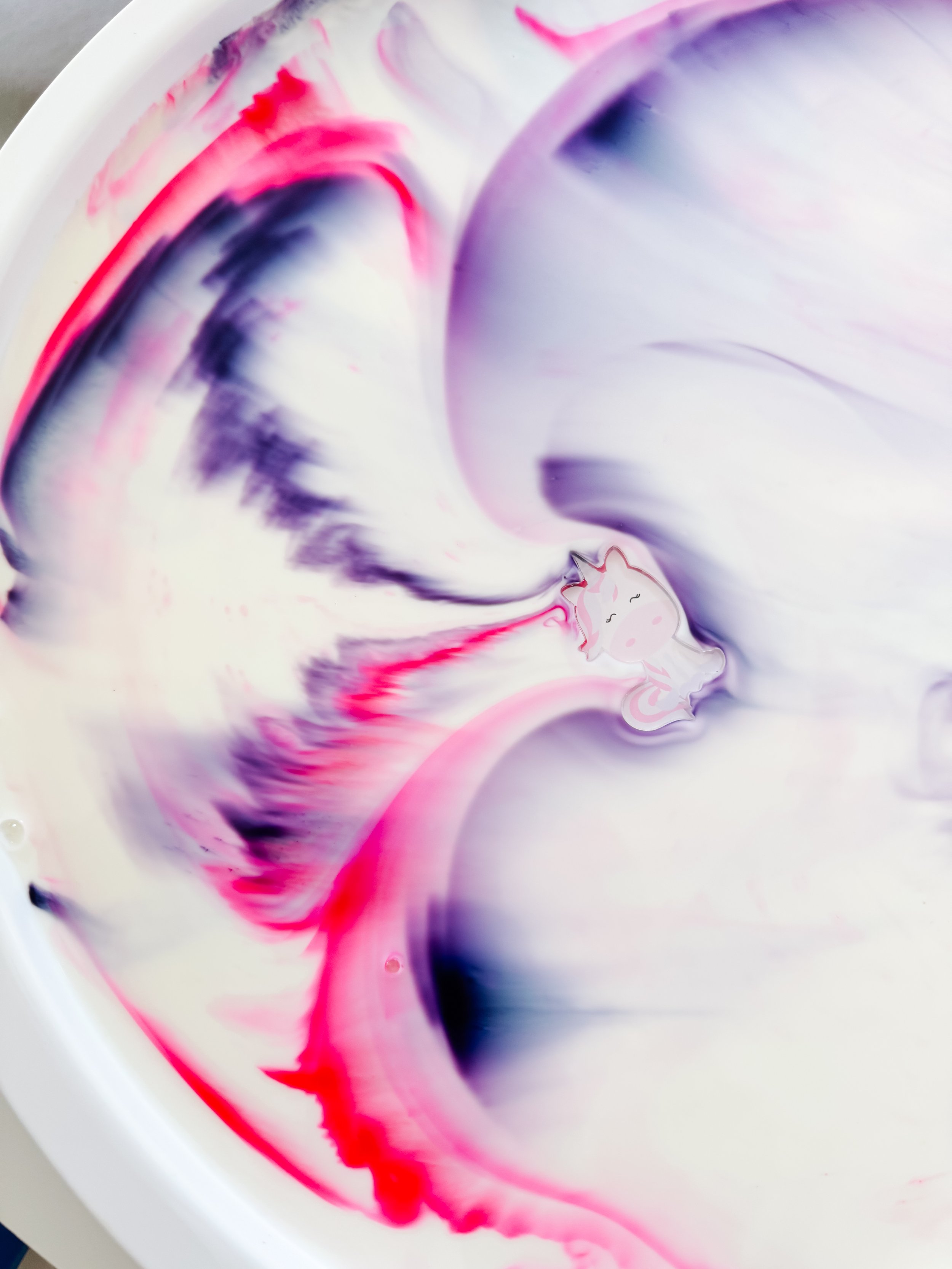 Unicorn acrylic charm floating among bright pink and purple Magic Milk swirls.