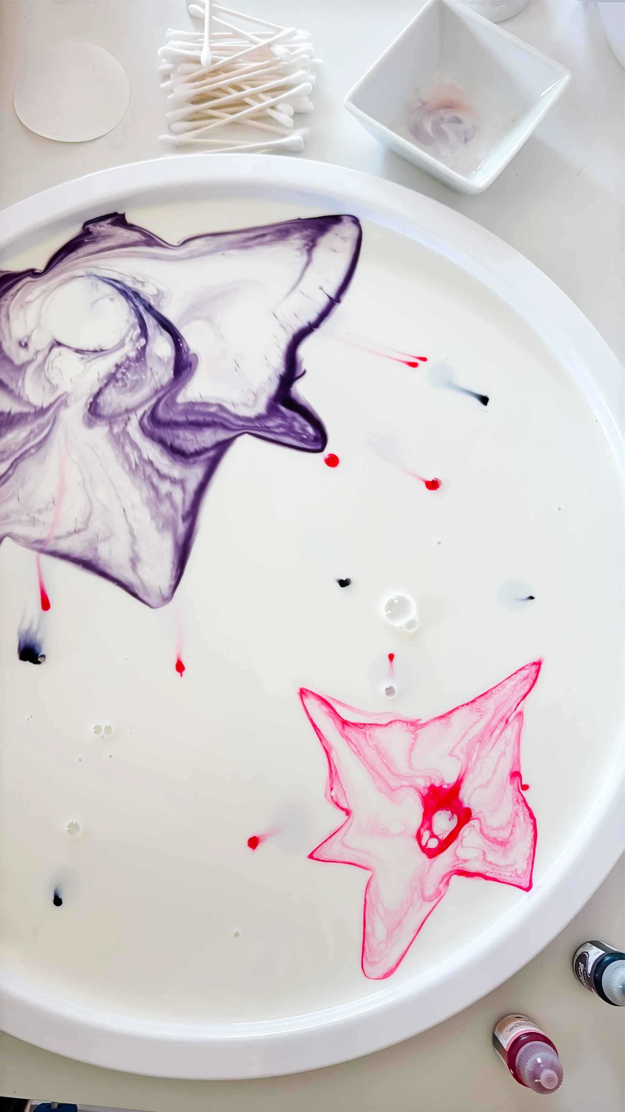 Pink and purple food coloring arranged in unicorn-inspired shapes on a tray of whole milk.