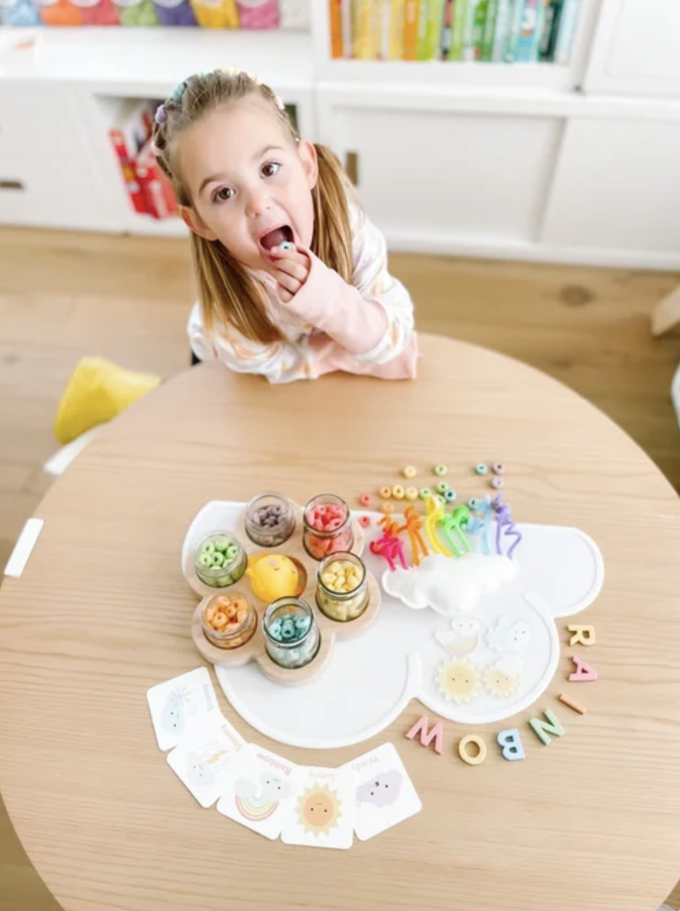 Child doing a rainbow cloud pipe cleaner and Fruit Loop craft with colorful cereal sorted in jars.