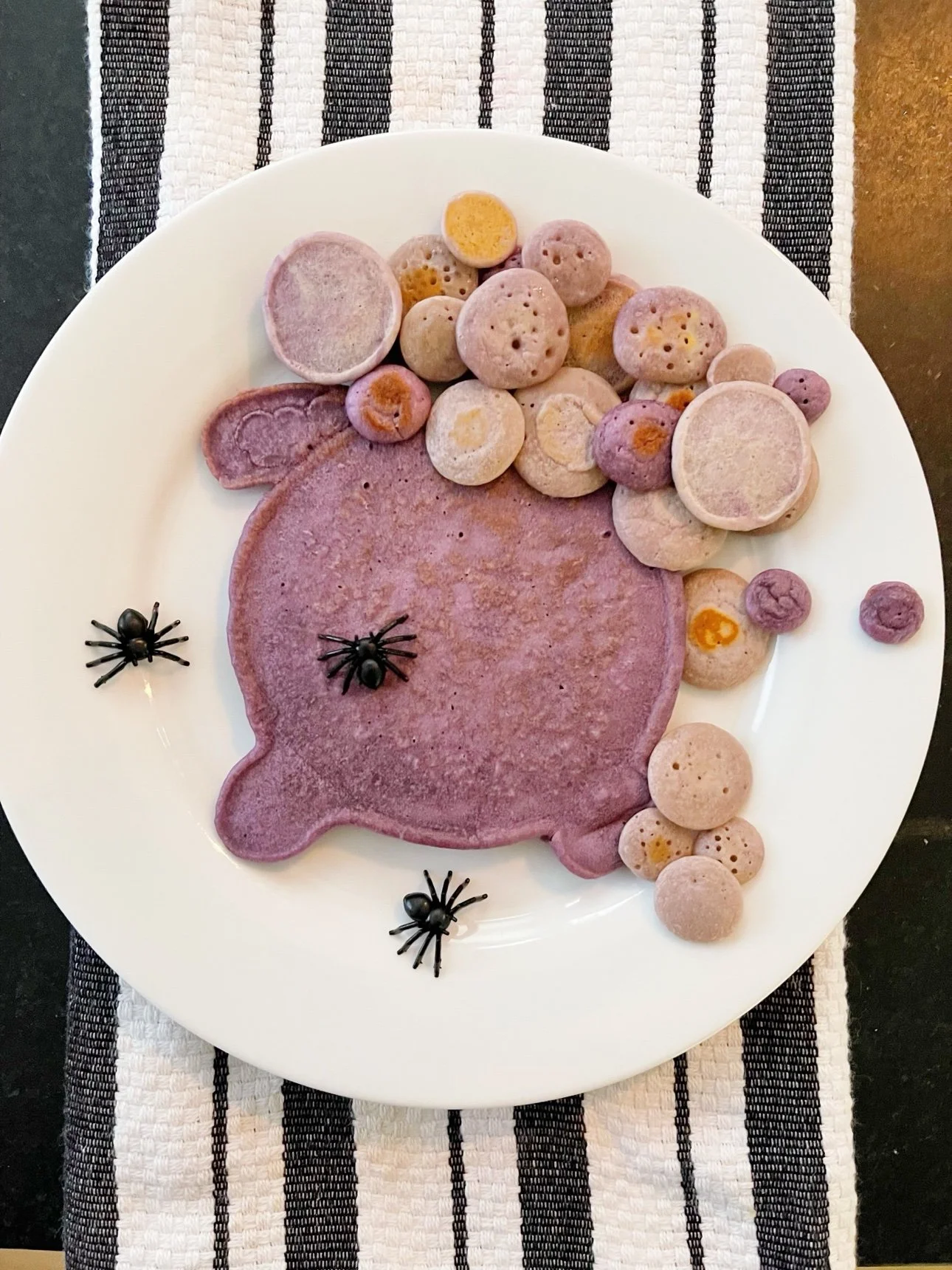 spider-shaped purple pancake art with mini pancakes and plastic spider decorations