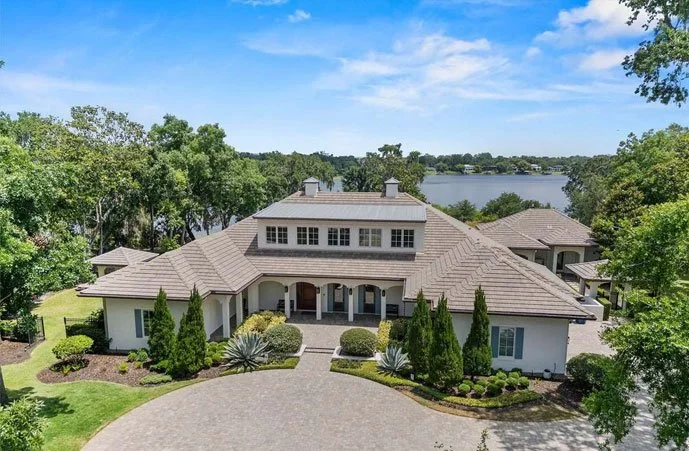 Large luxury home with manicured landscaping and lake view in the background under a clear blue sky in Winter Park, FL